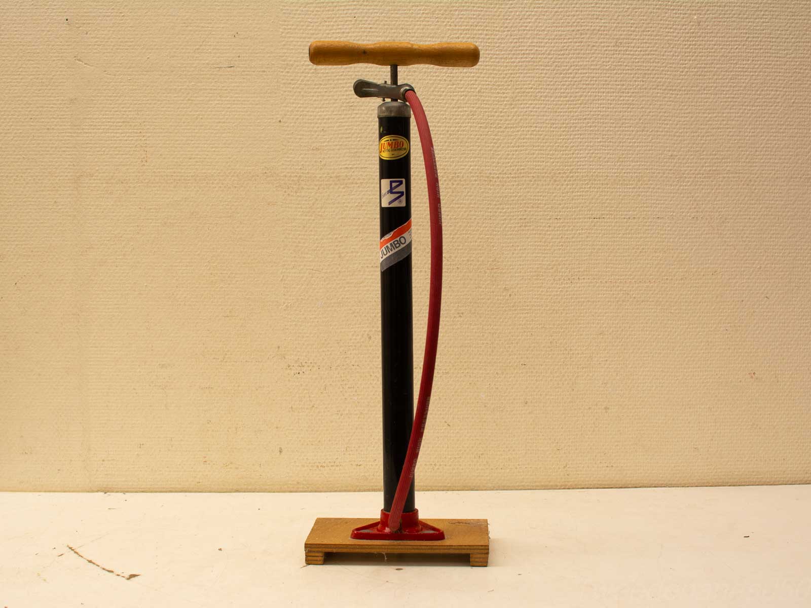 Vintage hand pump with wooden handle and red hose for inflating bikes and sports gear.