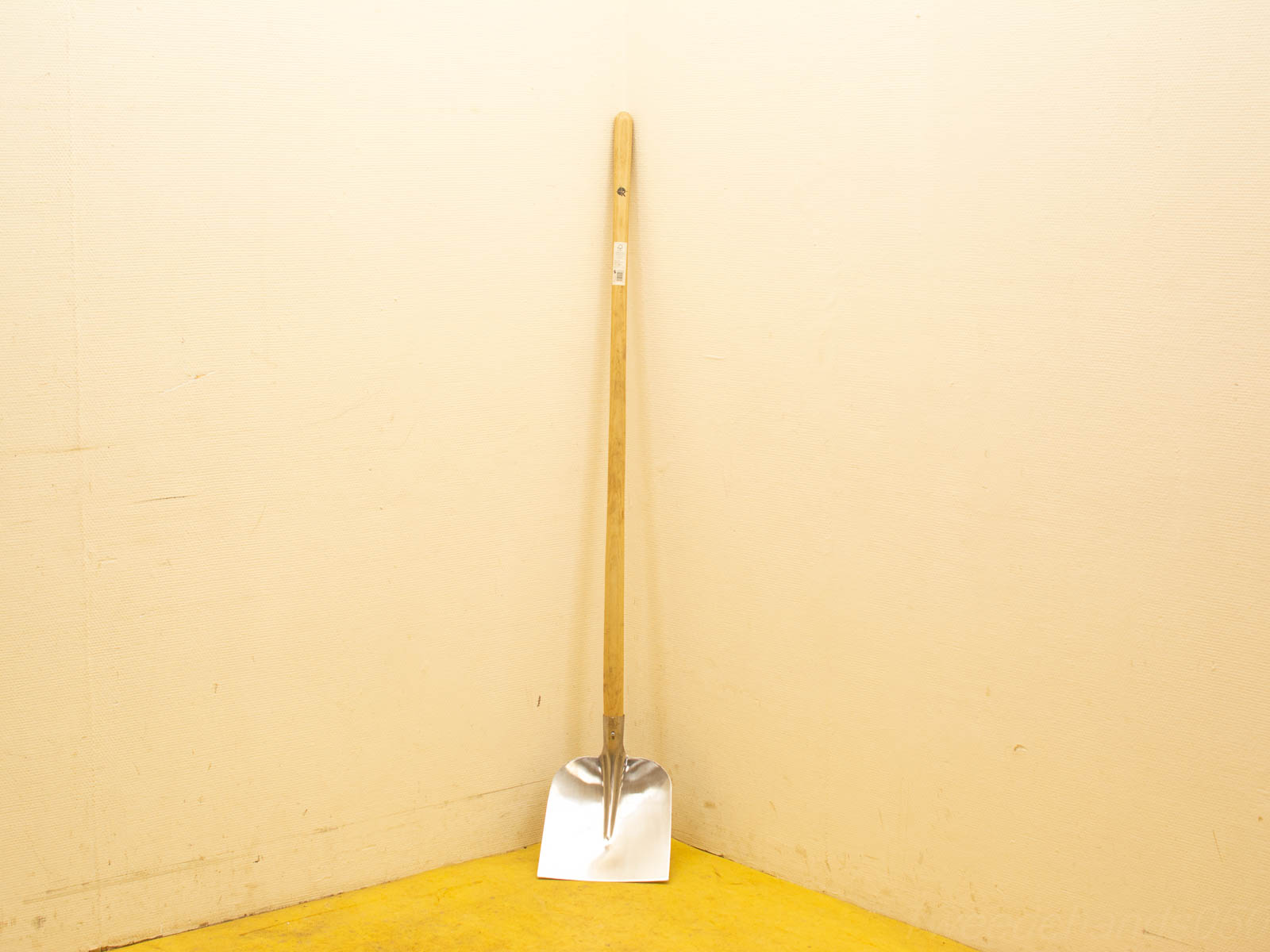 Sleek shovel in corner, wooden handle, vibrant yellow floor, perfect for outdoor tasks.