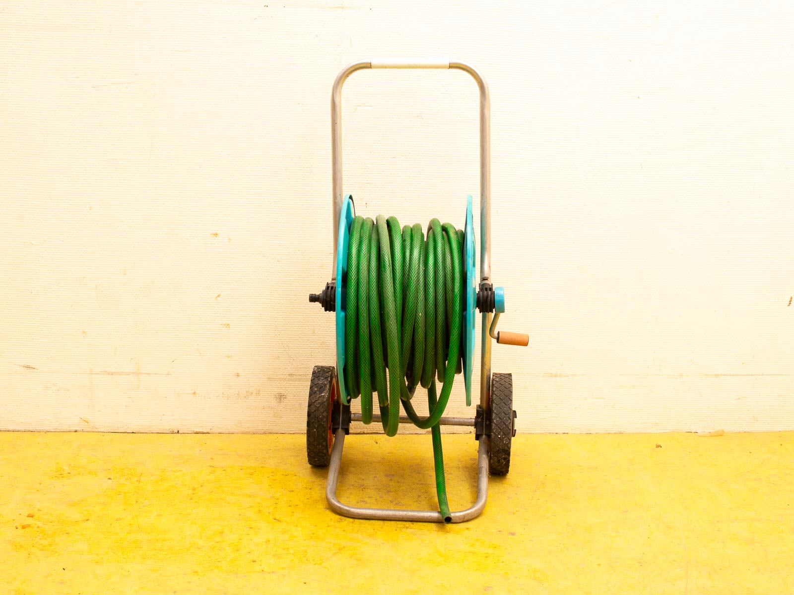 Durable garden hose reel with green hose, featuring wheels and a bright yellow floor.