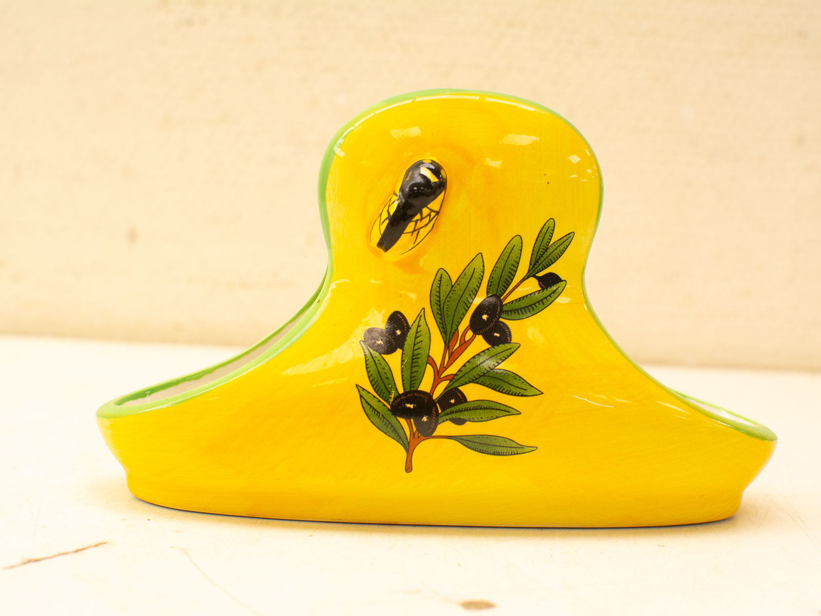 Bright yellow bird-shaped ceramic vase with green leaves and black berries, perfect for decor.