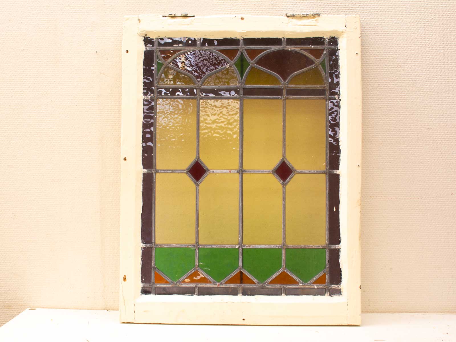 Vintage colorful geometric stained glass in weathered wooden frame, featuring red, yellow, and green hues.