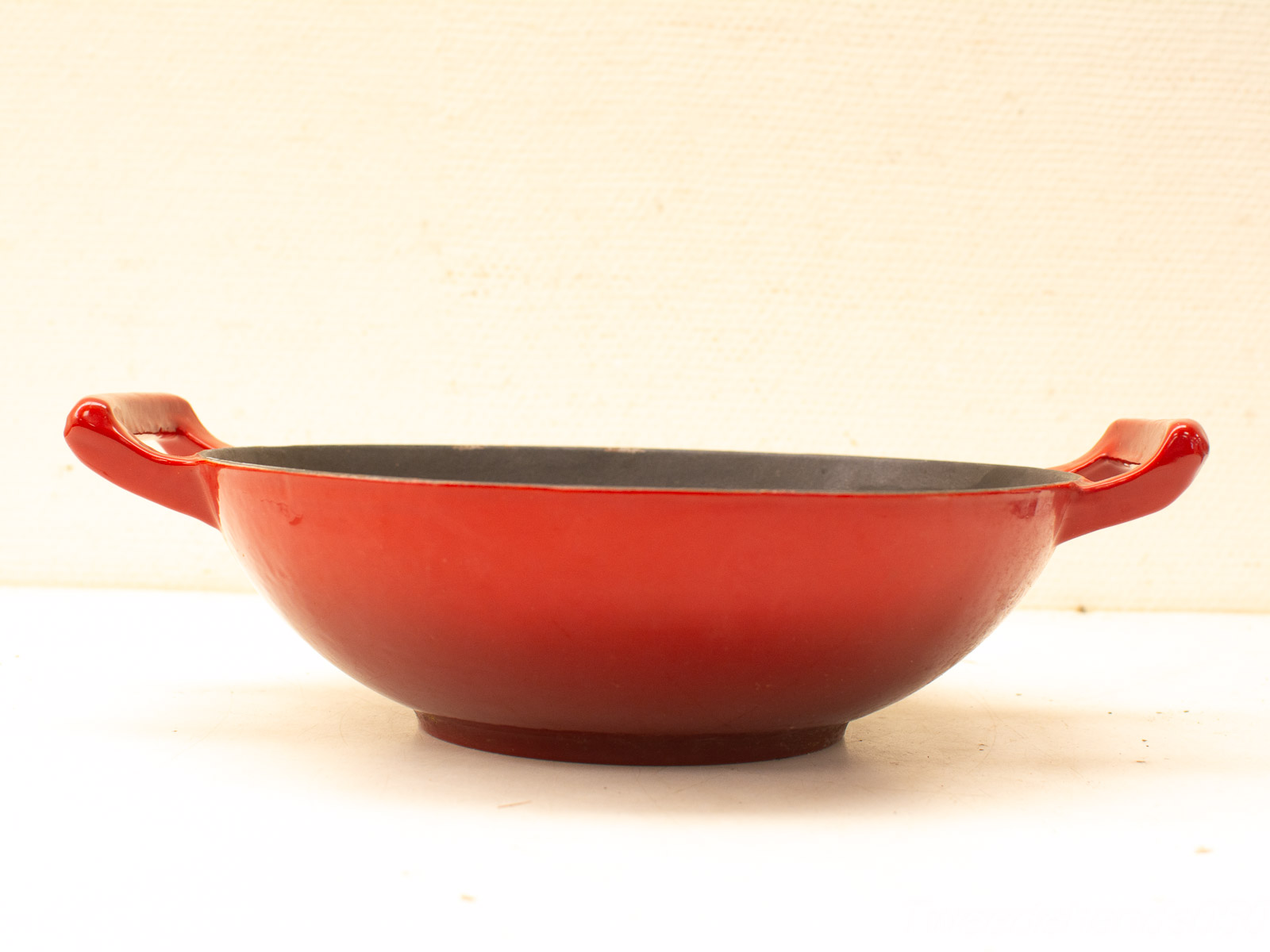 Red ceramic cooking pot with sturdy handles and non-stick dark gray interior, perfect for various culinary tasks.