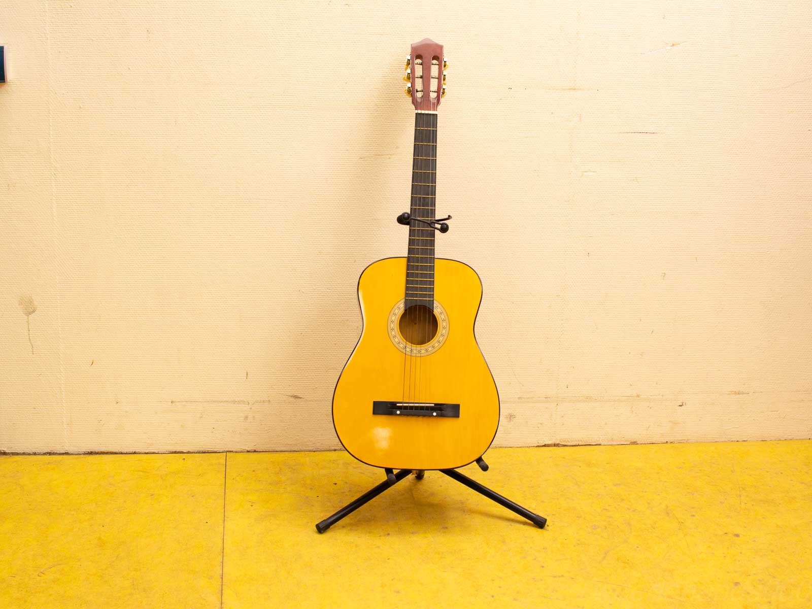 Classic yellow acoustic guitar on stand, ready for musical creativity against a beige backdrop.