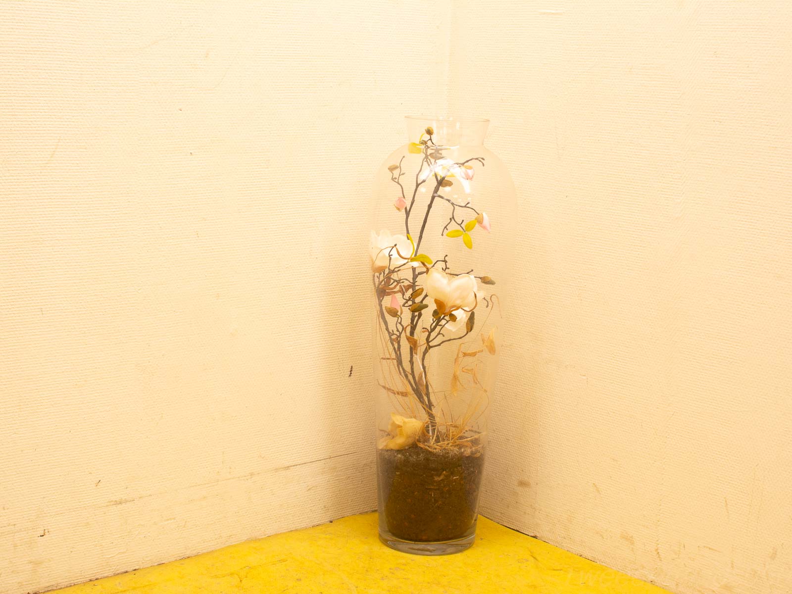 Elegant glass vase with soft artificial flowers on a cheerful yellow floor.