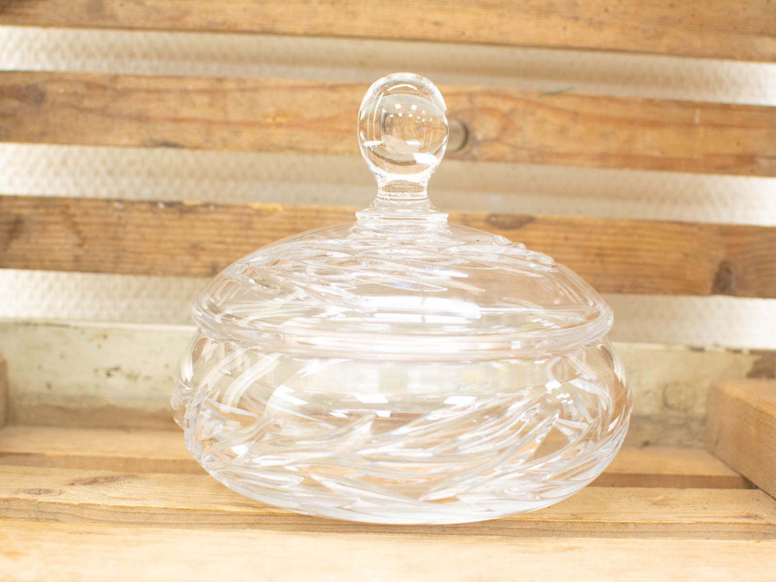 Elegant lidded glass jar with swirling design, set against a warm wooden background.