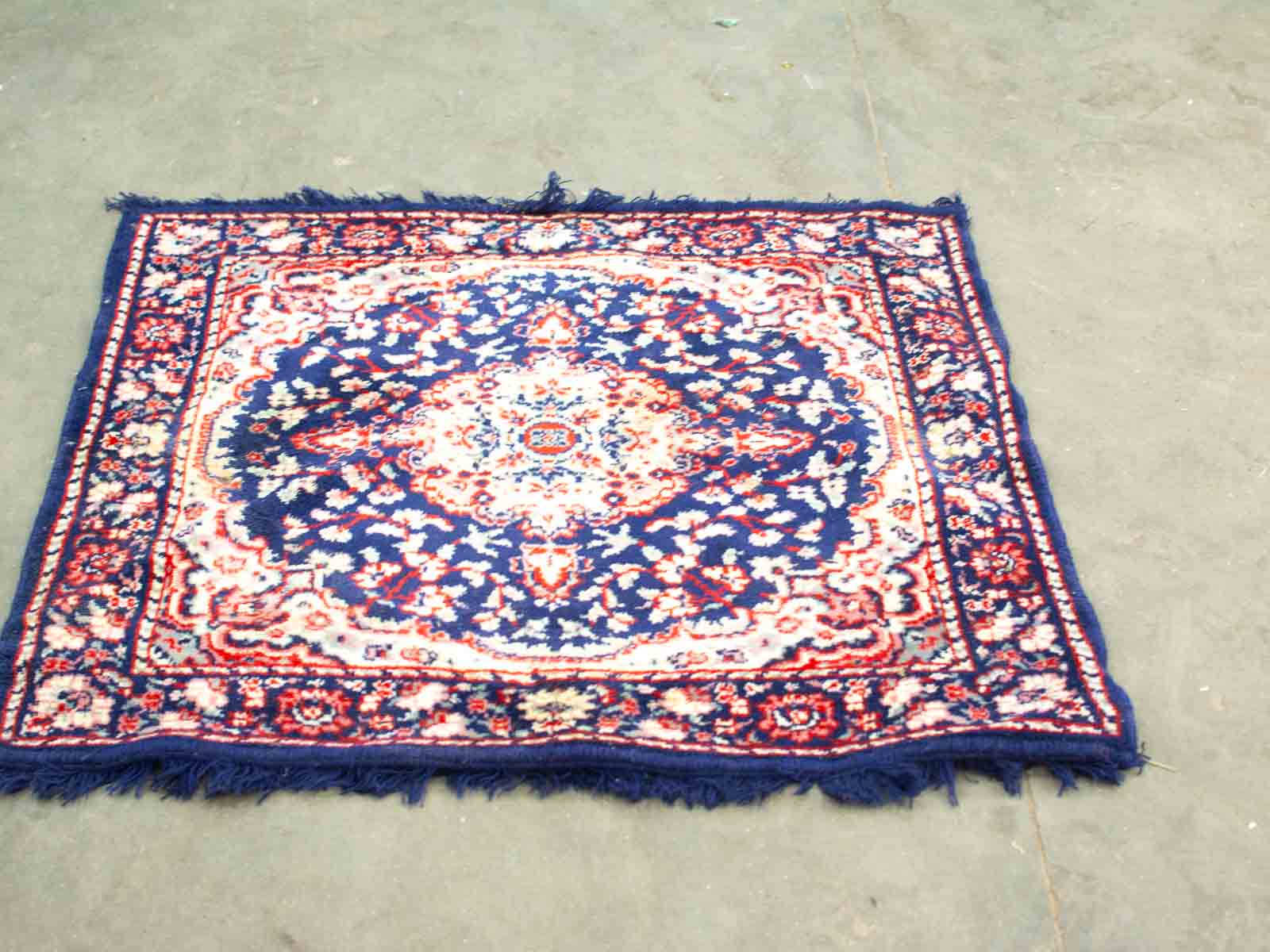 Handcrafted Navy Blue Area Rug with Floral Designs and Fringe on a Concrete Surface.