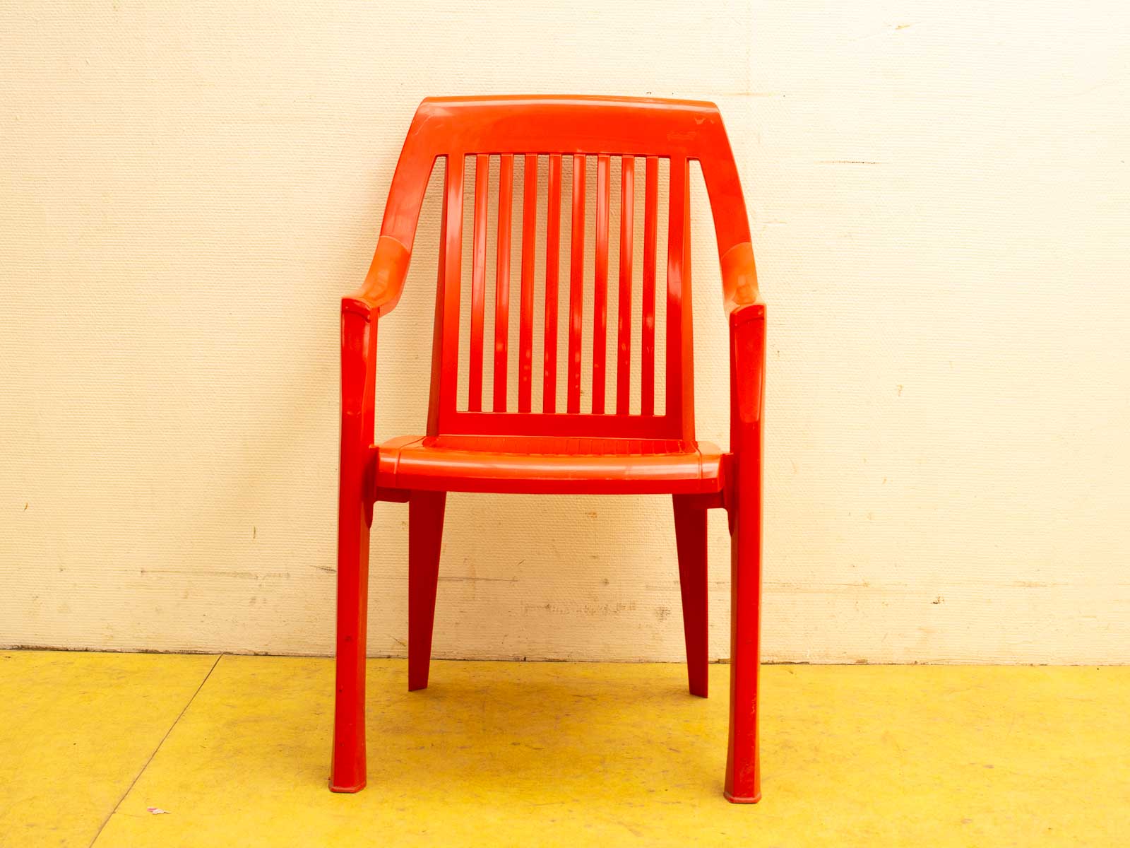 Bright red plastic chair on a cheerful yellow floor, perfect for modern indoor and outdoor spaces.