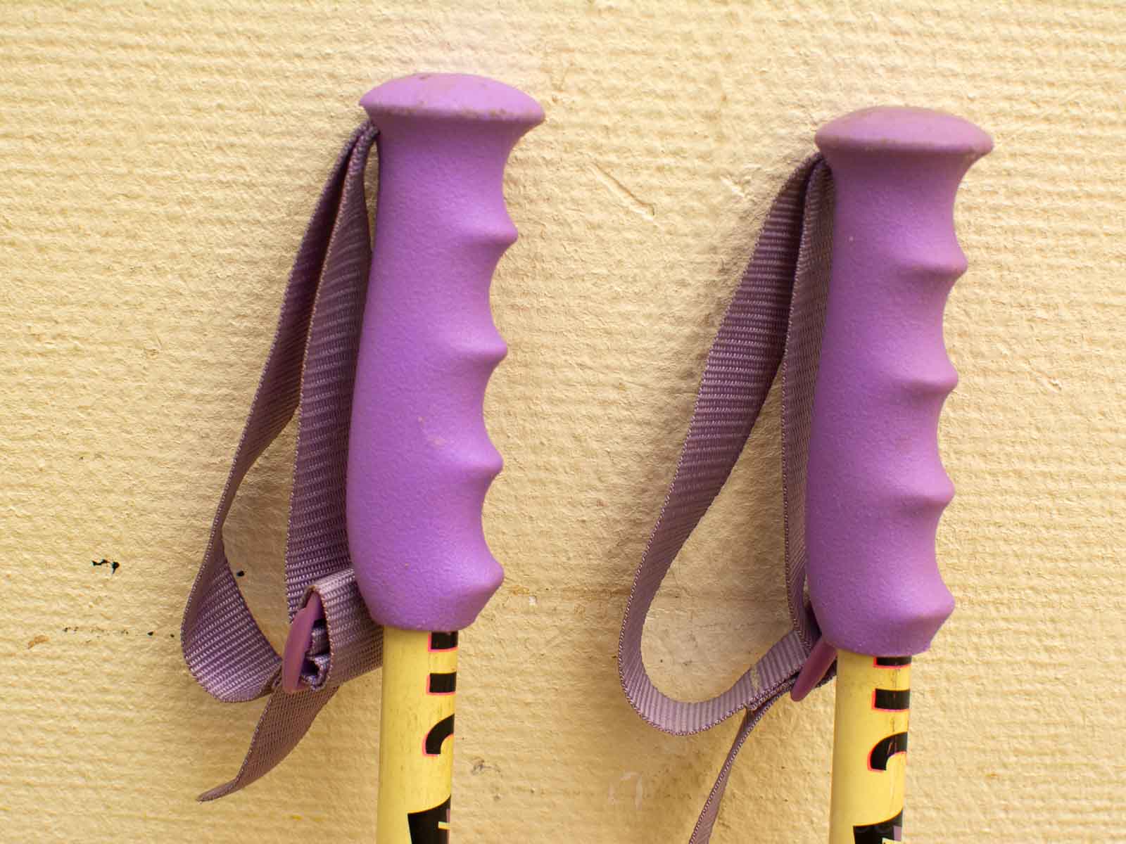 Vibrant purple-gripped hiking poles resting against a textured yellow wall, ready for adventure.