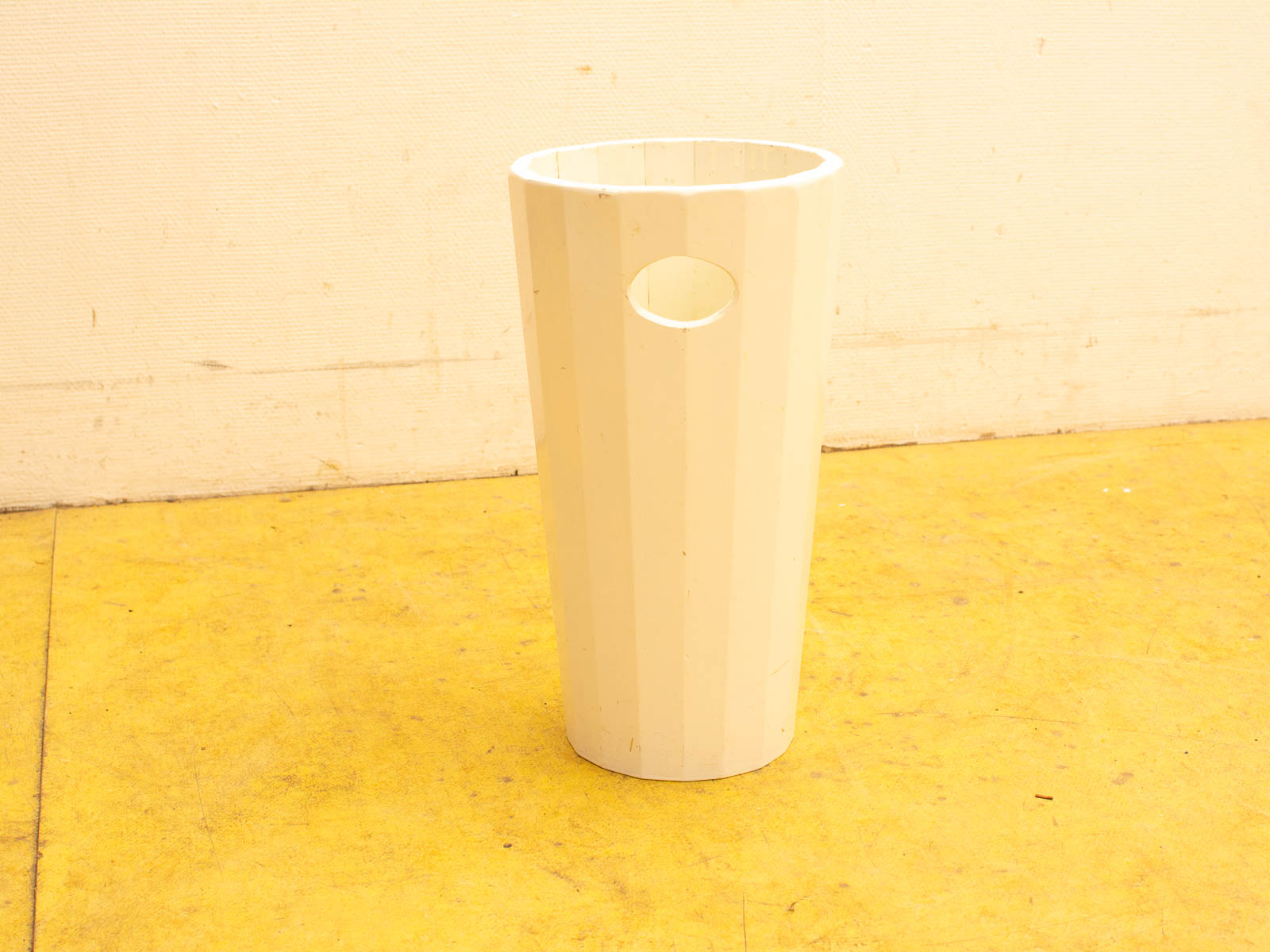 Sleek white cylindrical container with ridges, set on a vibrant yellow floor.