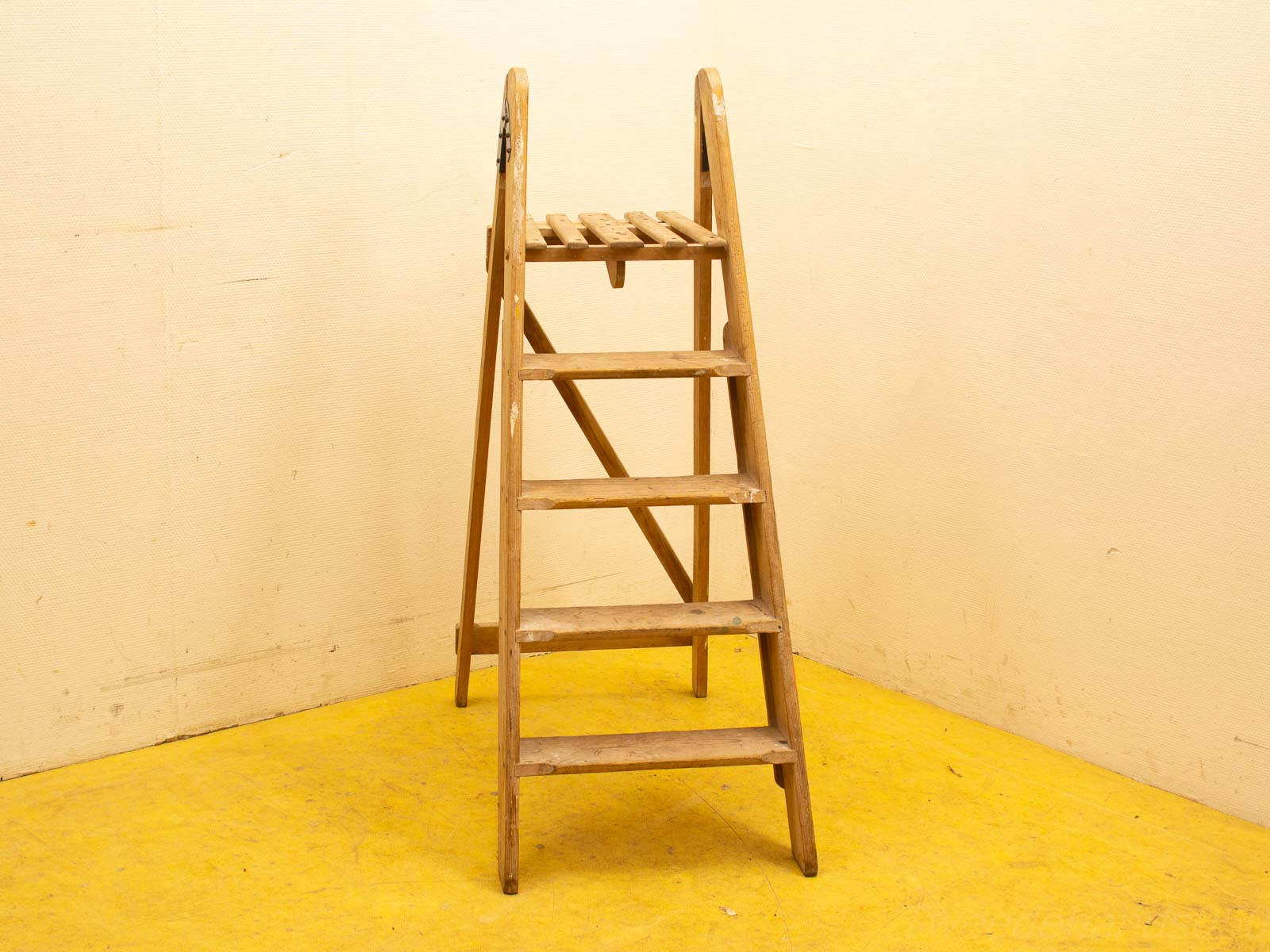 Vintage wooden step ladder with paint splatters, against a pale yellow wall, used for DIY projects.