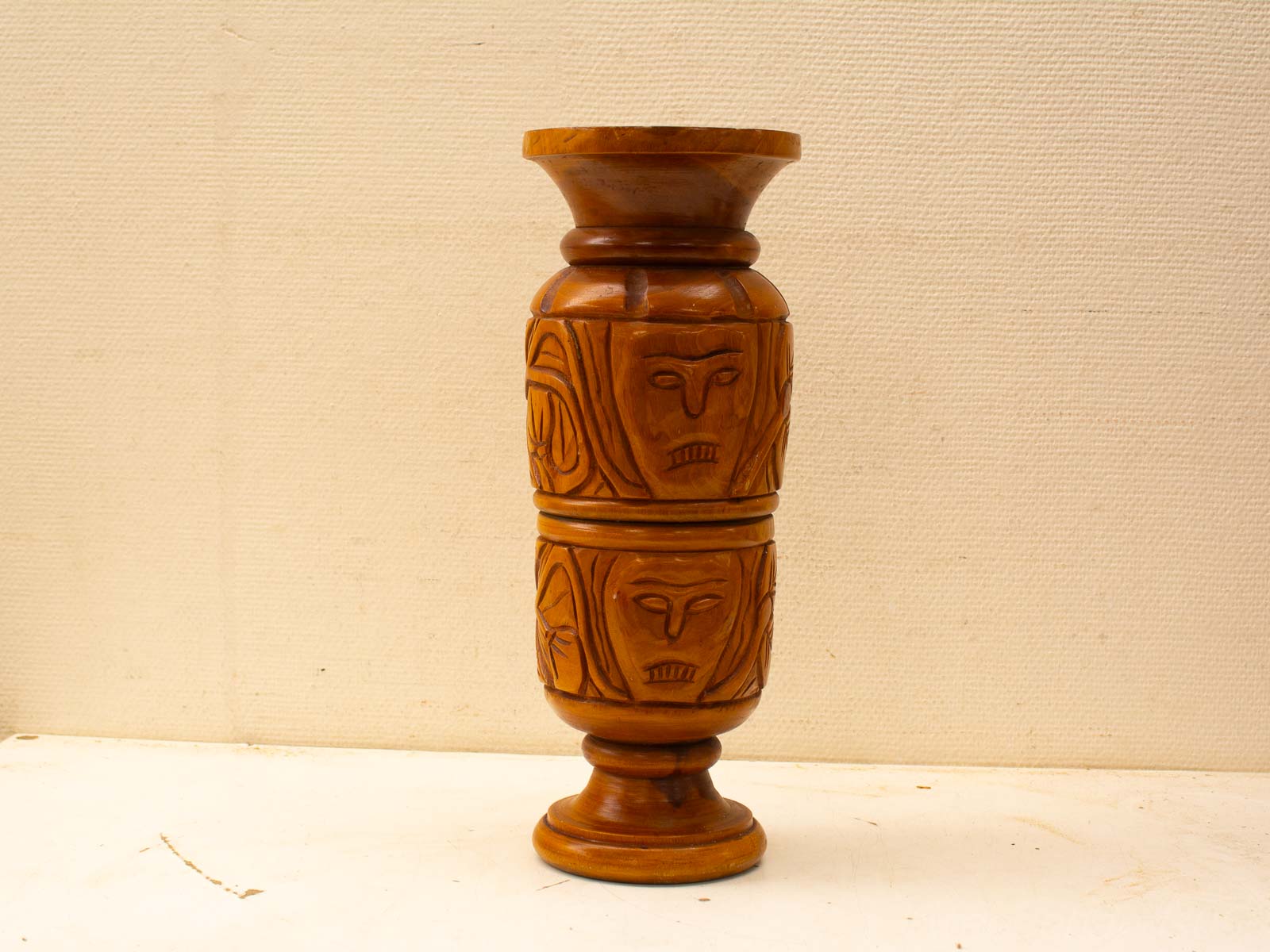 Handcrafted wooden vase with detailed face carvings, highlighting traditional art on a neutral backdrop.