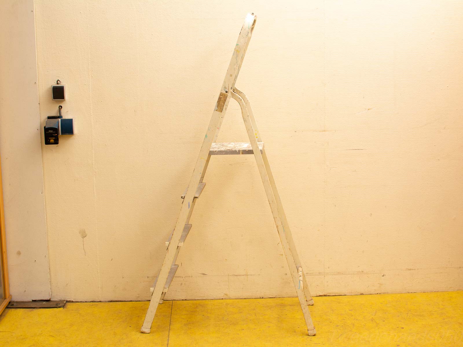 Used white ladder in a functional workspace with cream wall and vibrant yellow floor.