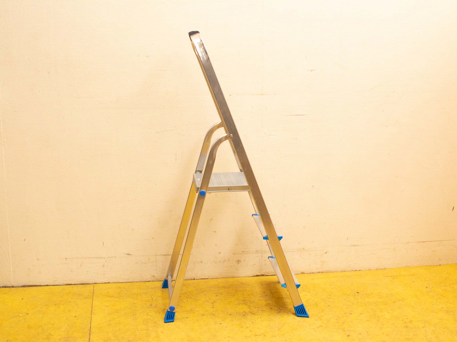 Modern aluminum step ladder with textured steps and rubber feet against a light wall.