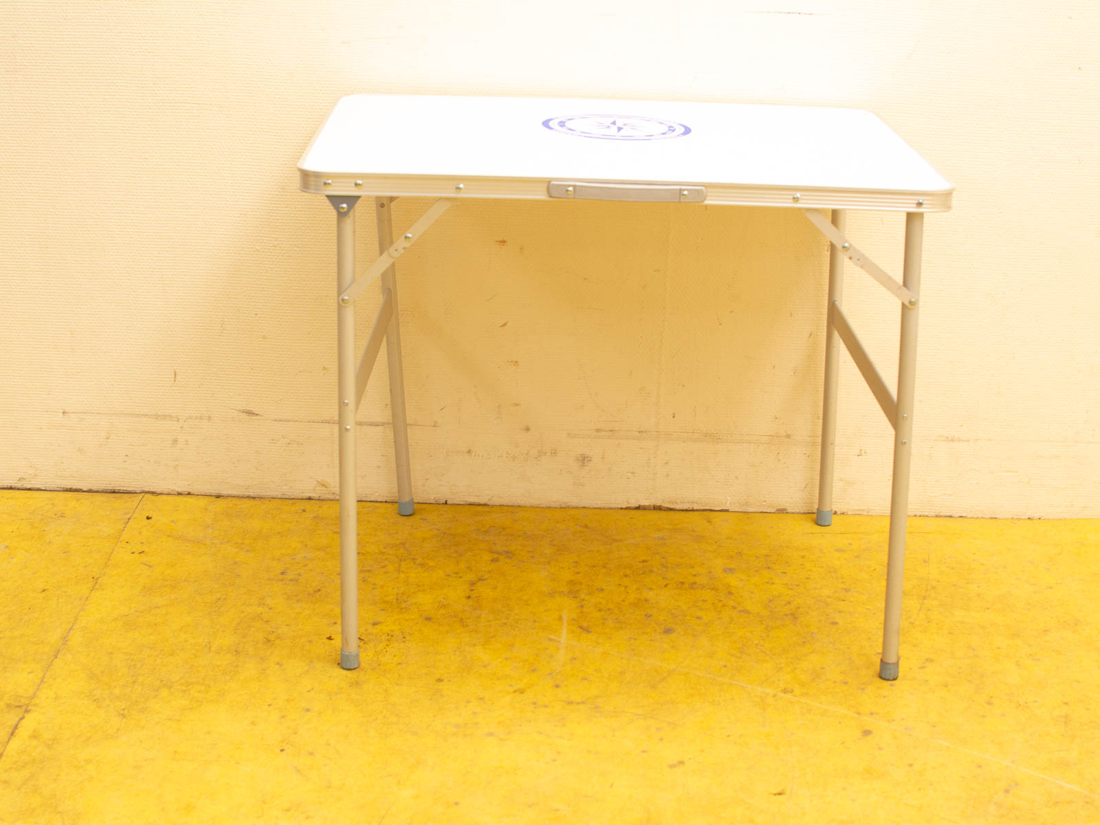 Foldable white table with blue design on vibrant yellow floor, ideal for versatile use.