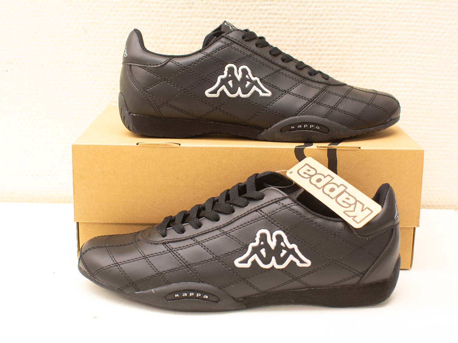 Stylish black Kappa sneakers on a simple brown box, ideal for casual and sporty looks.