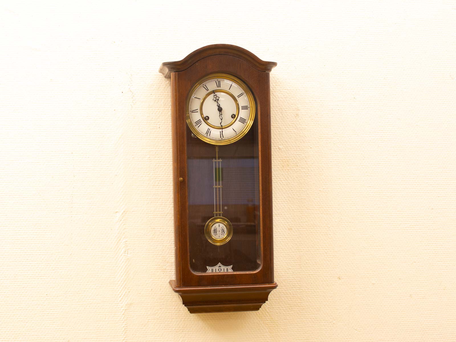 Elegant vintage wooden clock with Roman numerals and visible pendulum, perfect for any interior.