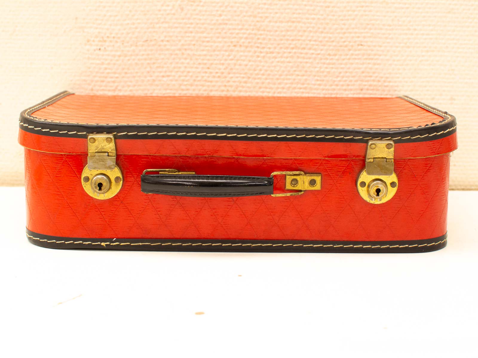 Charming vintage red suitcase with leather trim, brass locks, and quilted design for timeless elegance.