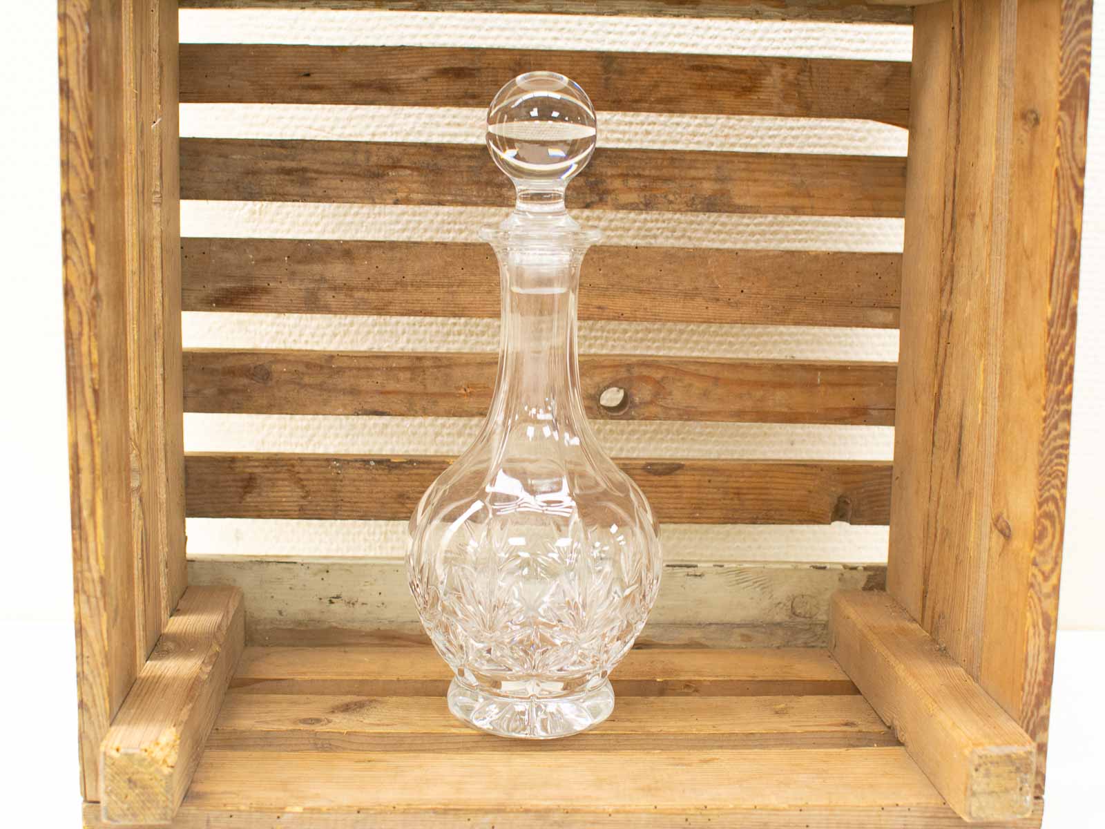 Elegant crystal decanter with intricate etching, displayed in rustic wooden crate, exuding sophistication and charm.