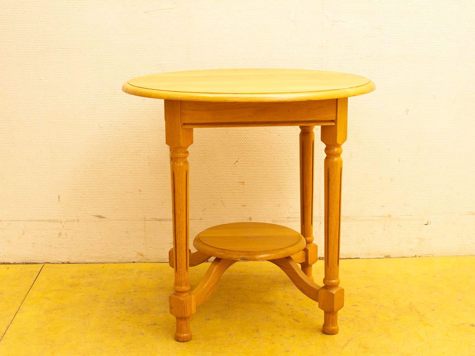 Light wooden round table with polished finish, sturdy legs, and extra storage shelf.