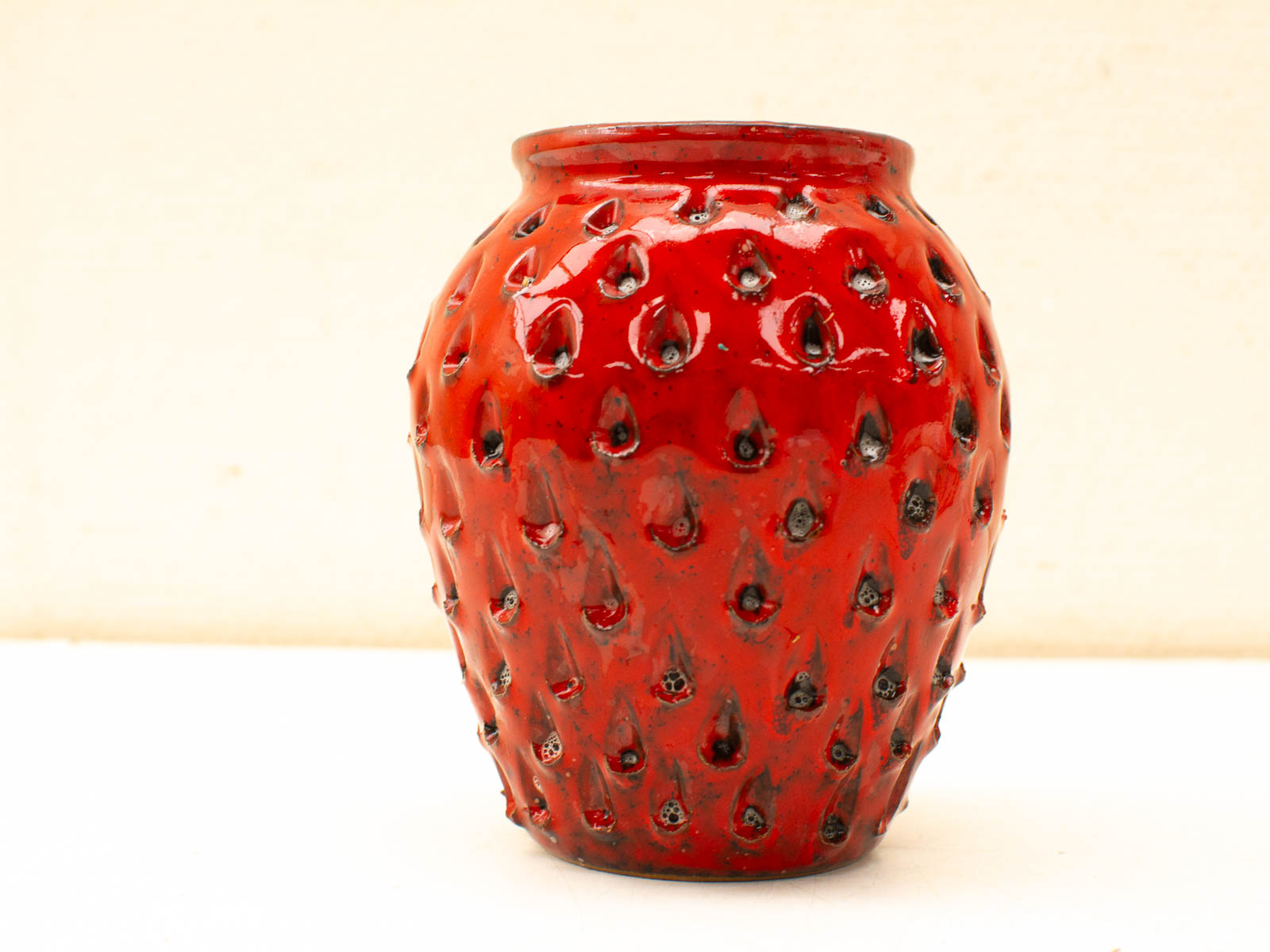 Whimsical strawberry ceramic vase with vibrant red glaze, perfect for brightening any decor.