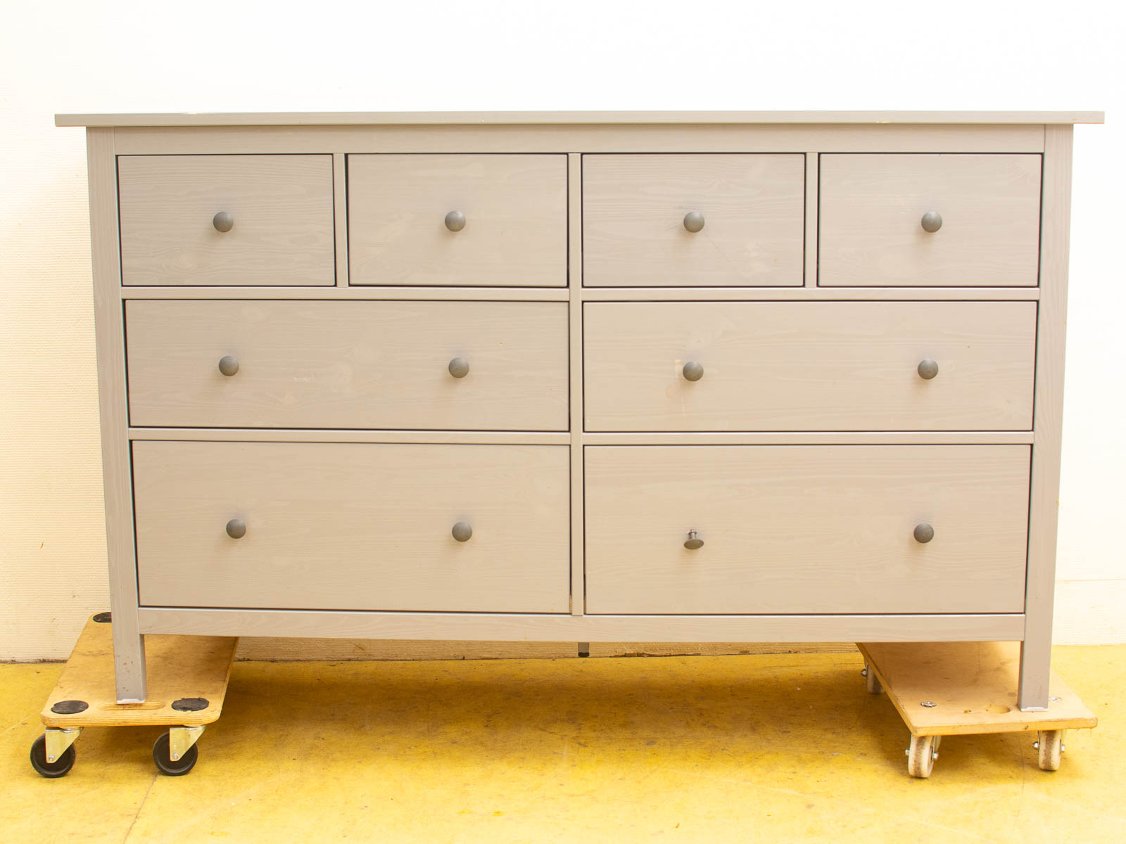 Modern light gray dresser with eight drawers and wheels, perfect for stylish, functional storage.