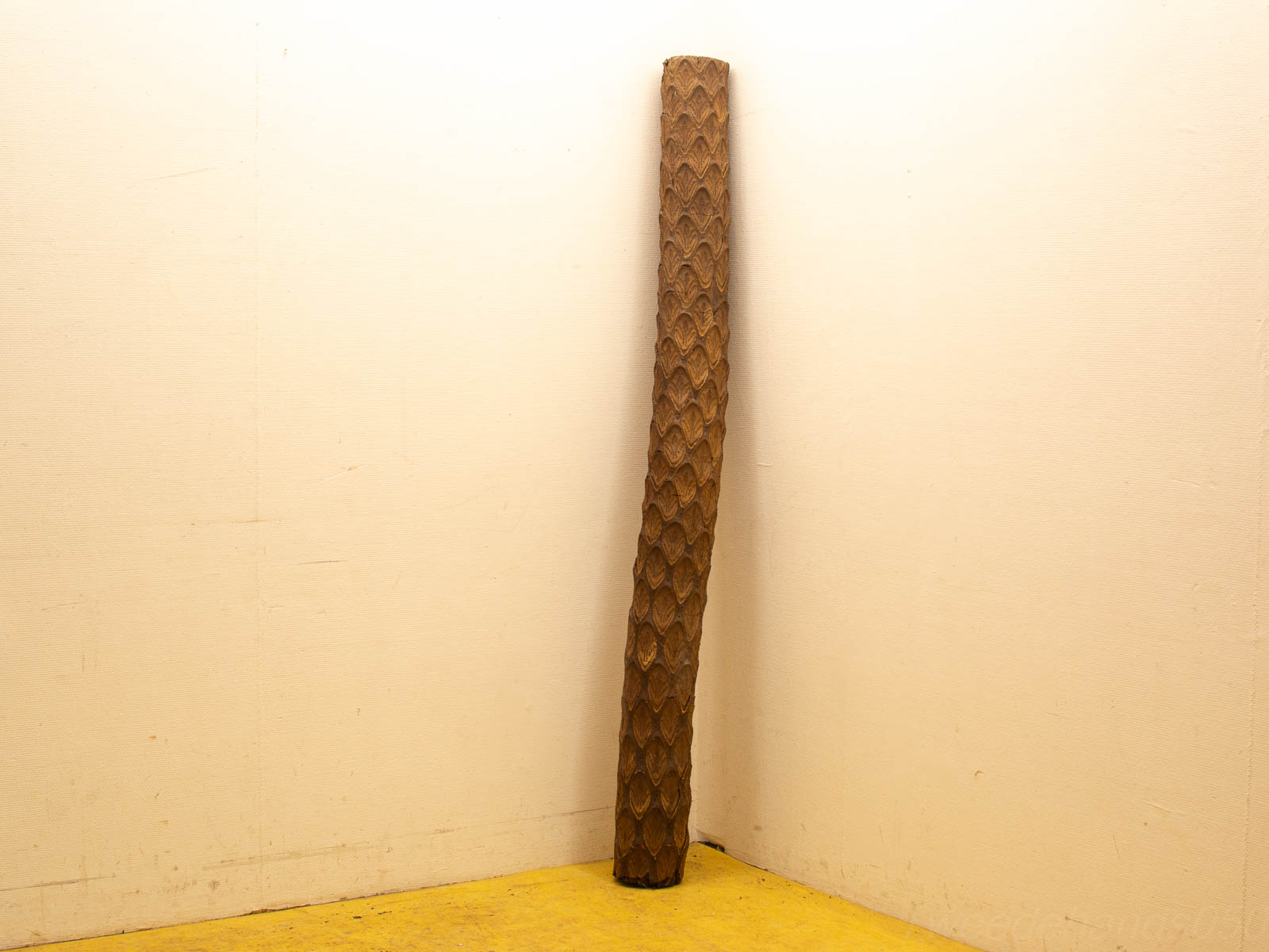 Unique wooden pole with scale pattern, warm tones, stylish décor against light wall and yellow floor.