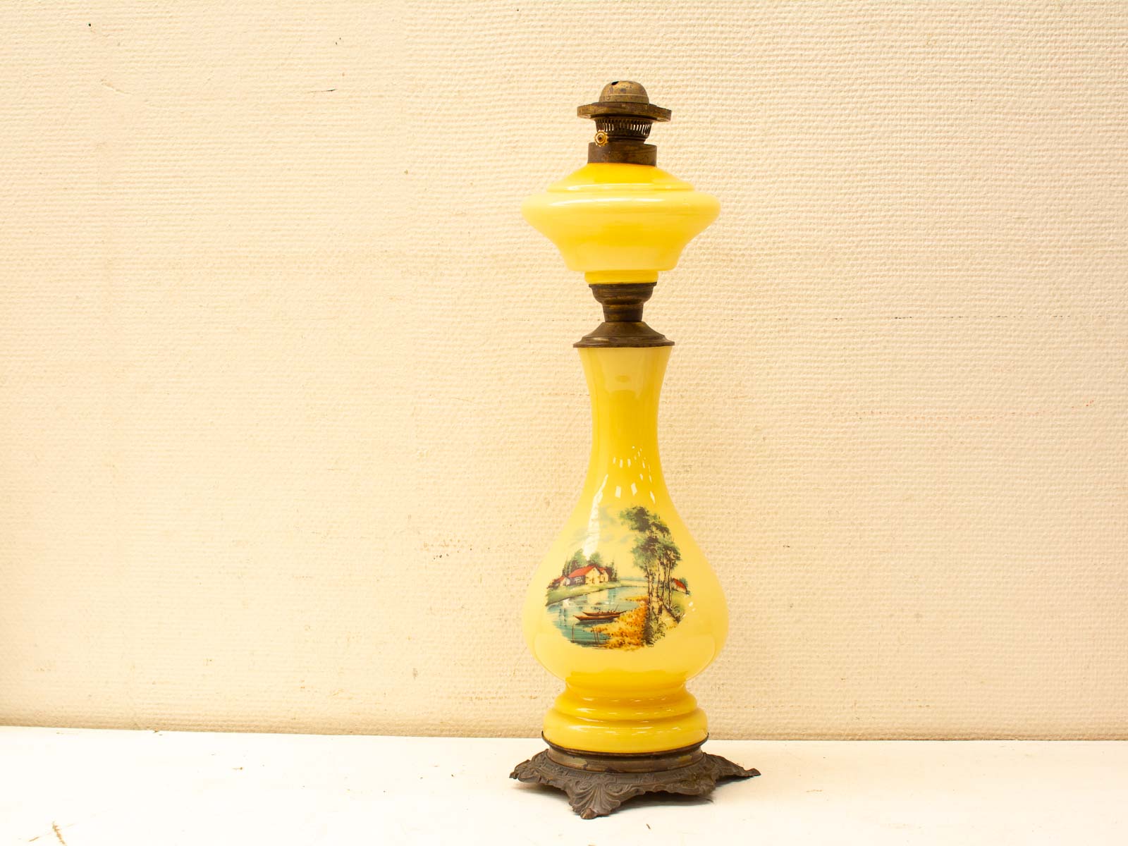 Charming vintage yellow oil lamp with landscape painting, elegant design, and ornate metal base.