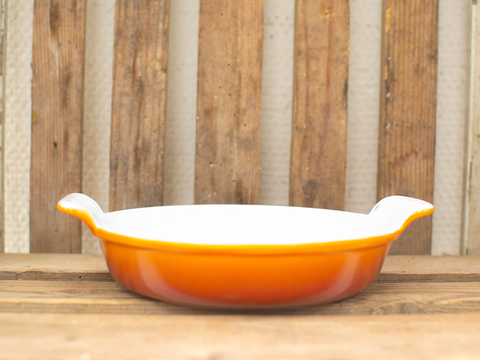 Orange ceramic baking dish with handles on rustic wooden background, perfect for home cooking.