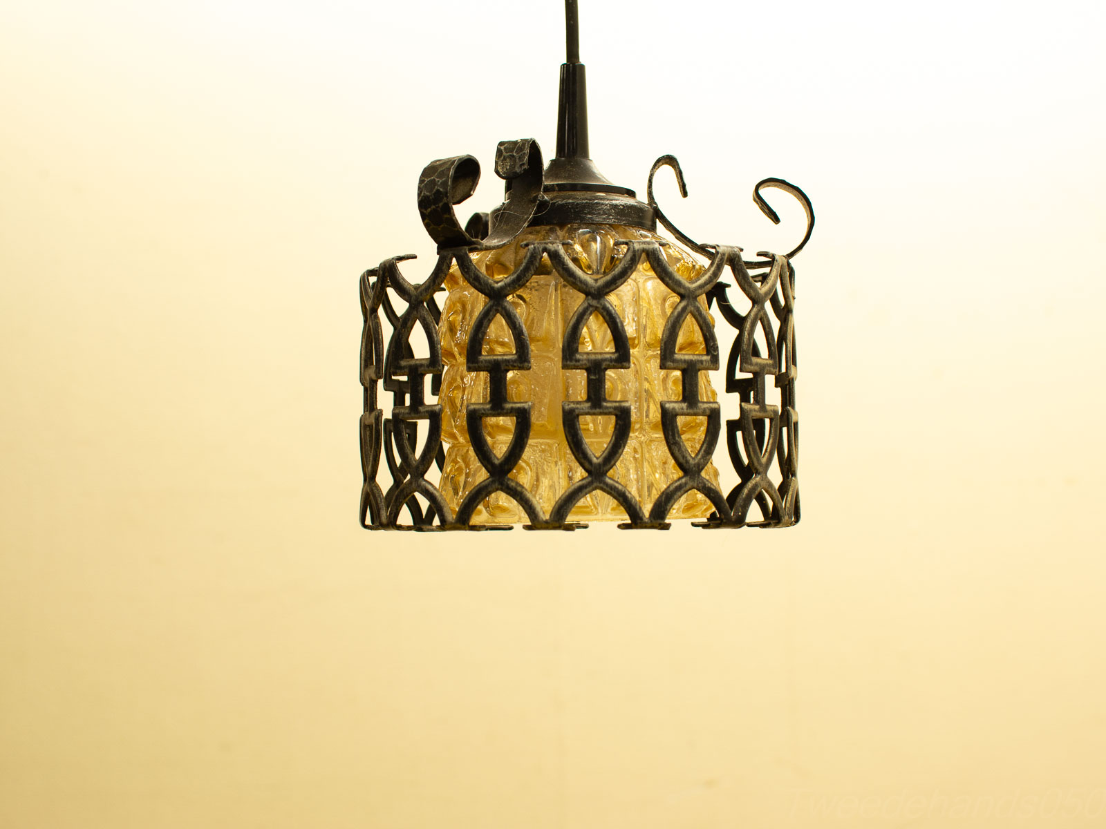 Elegant pendant lamp with textured amber glass and intricate wrought iron frame, perfect for cozy spaces.