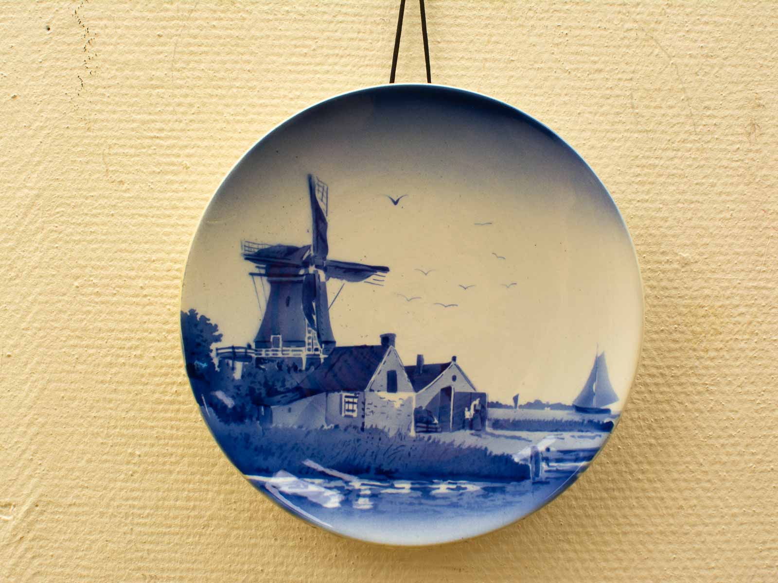 Rustic wall plate with windmill landscape, cottages, and sailboats in classic blue and white.