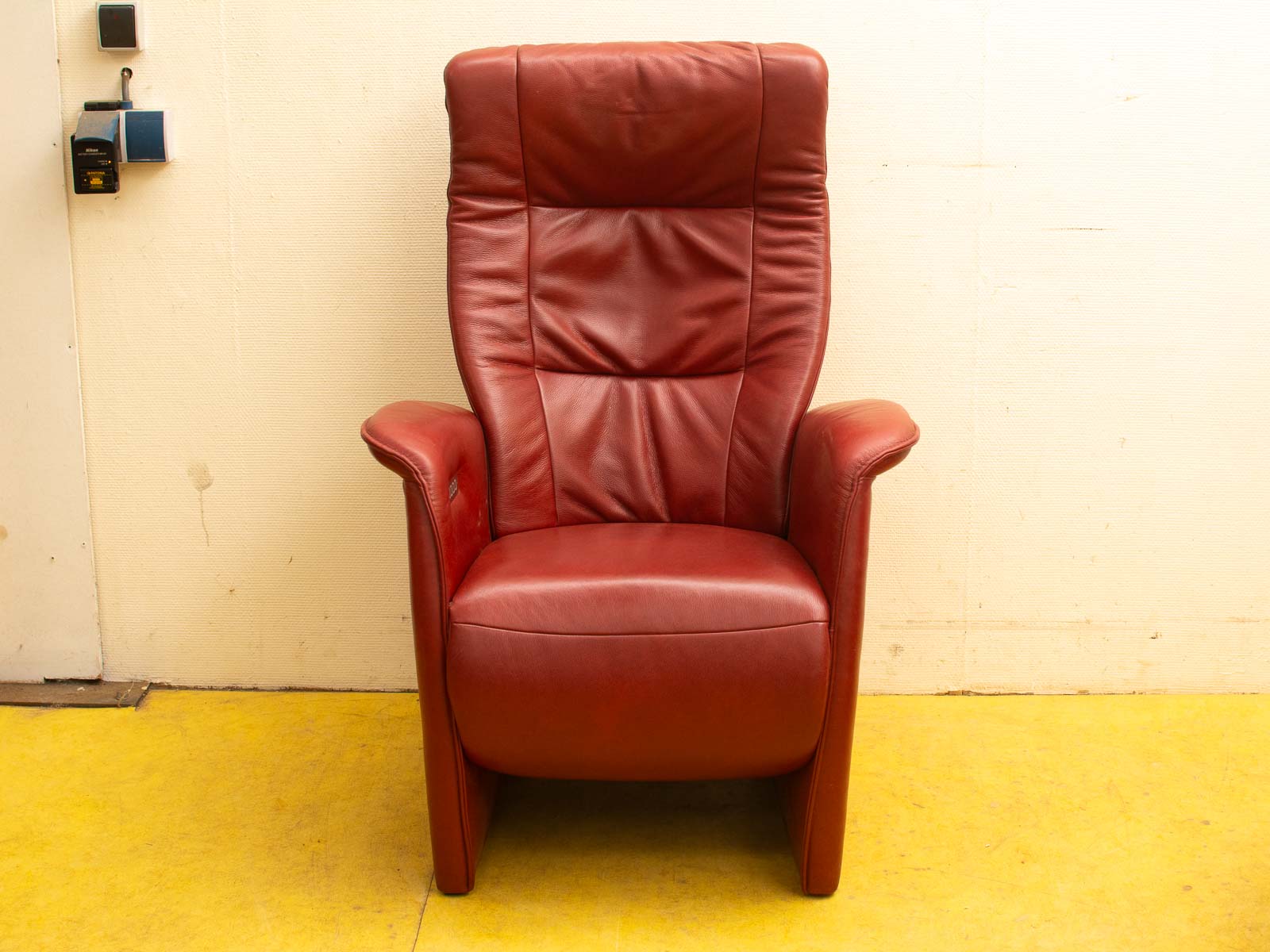 Striking red leather armchair featuring a modern design, high backrest and curved armrests in a stylish room.