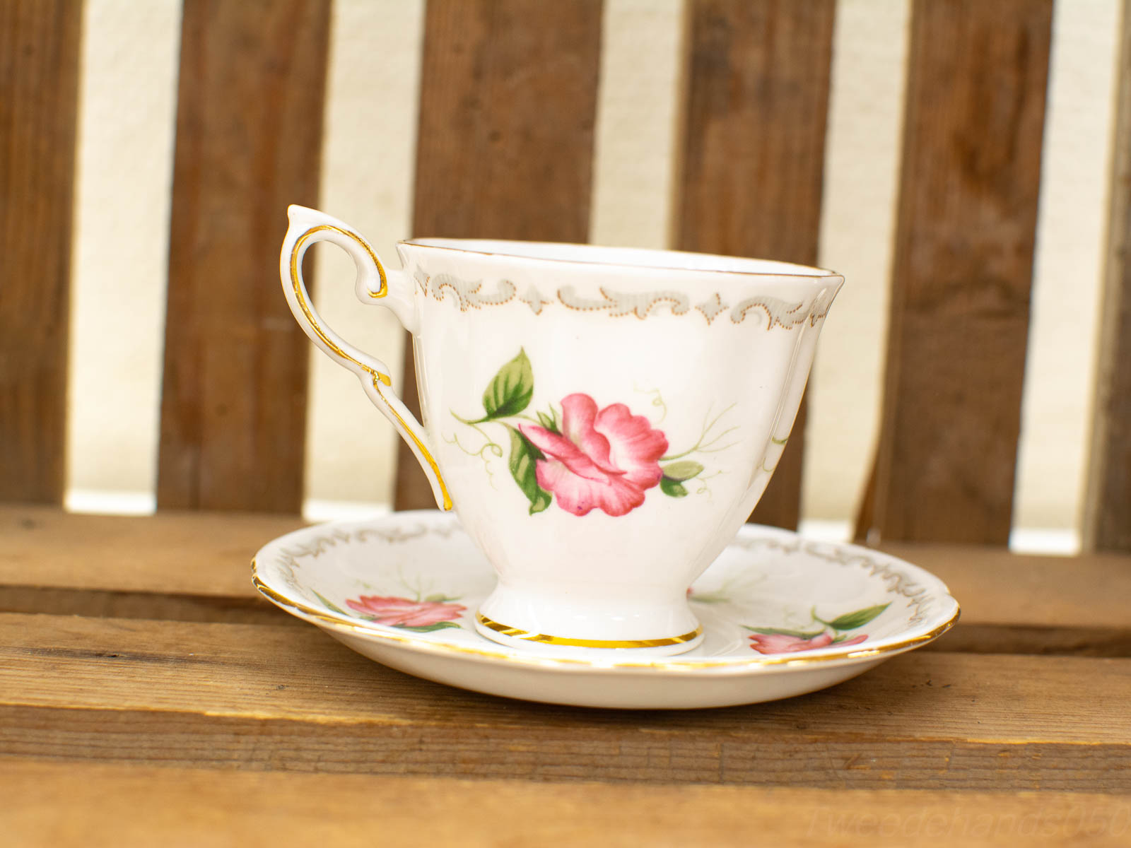 Elegant porcelain teacup and saucer with pink roses and gold accents on rustic wood.