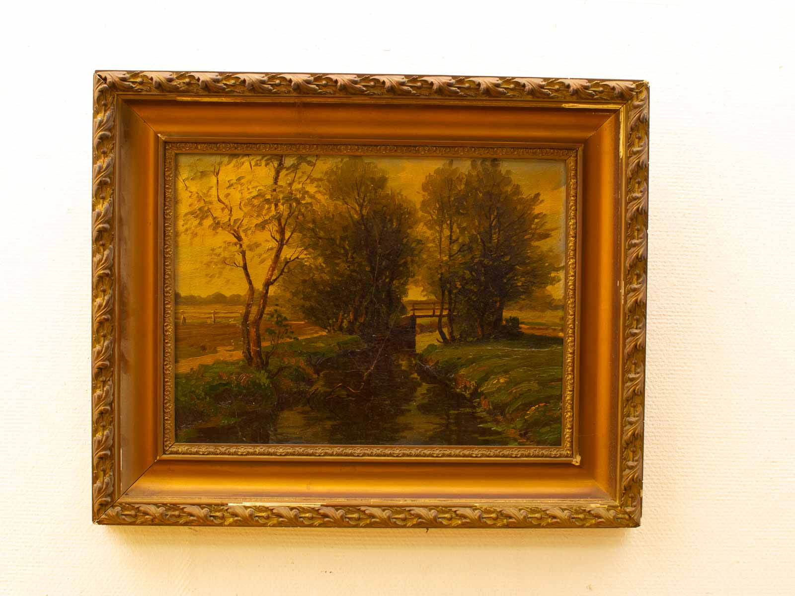 Serene landscape painting featuring a stream, trees, and wildflowers in an ornate golden frame.