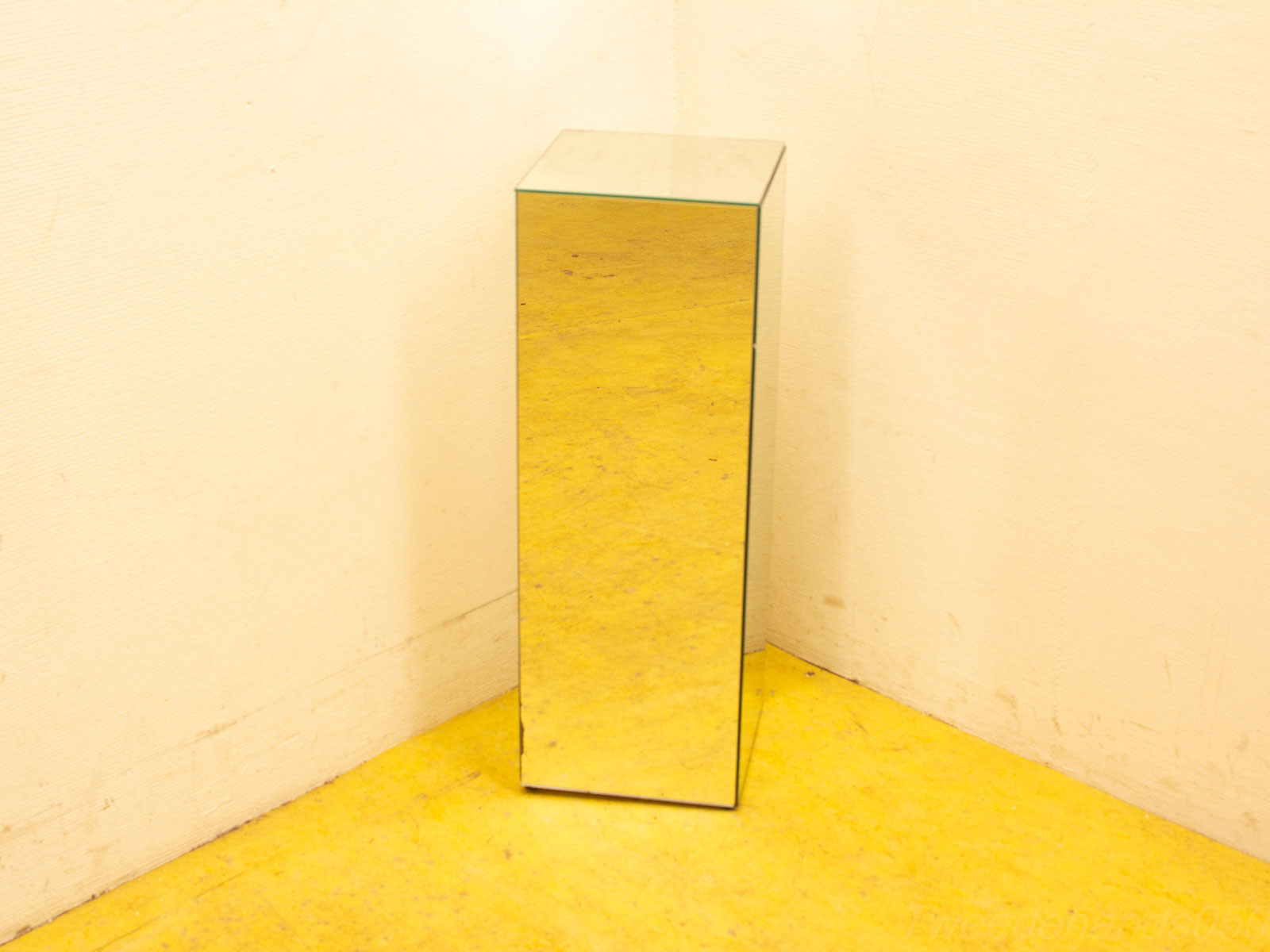 Sleek mirrored pedestal enhances modern yellow room with elegance and vibrant reflections.