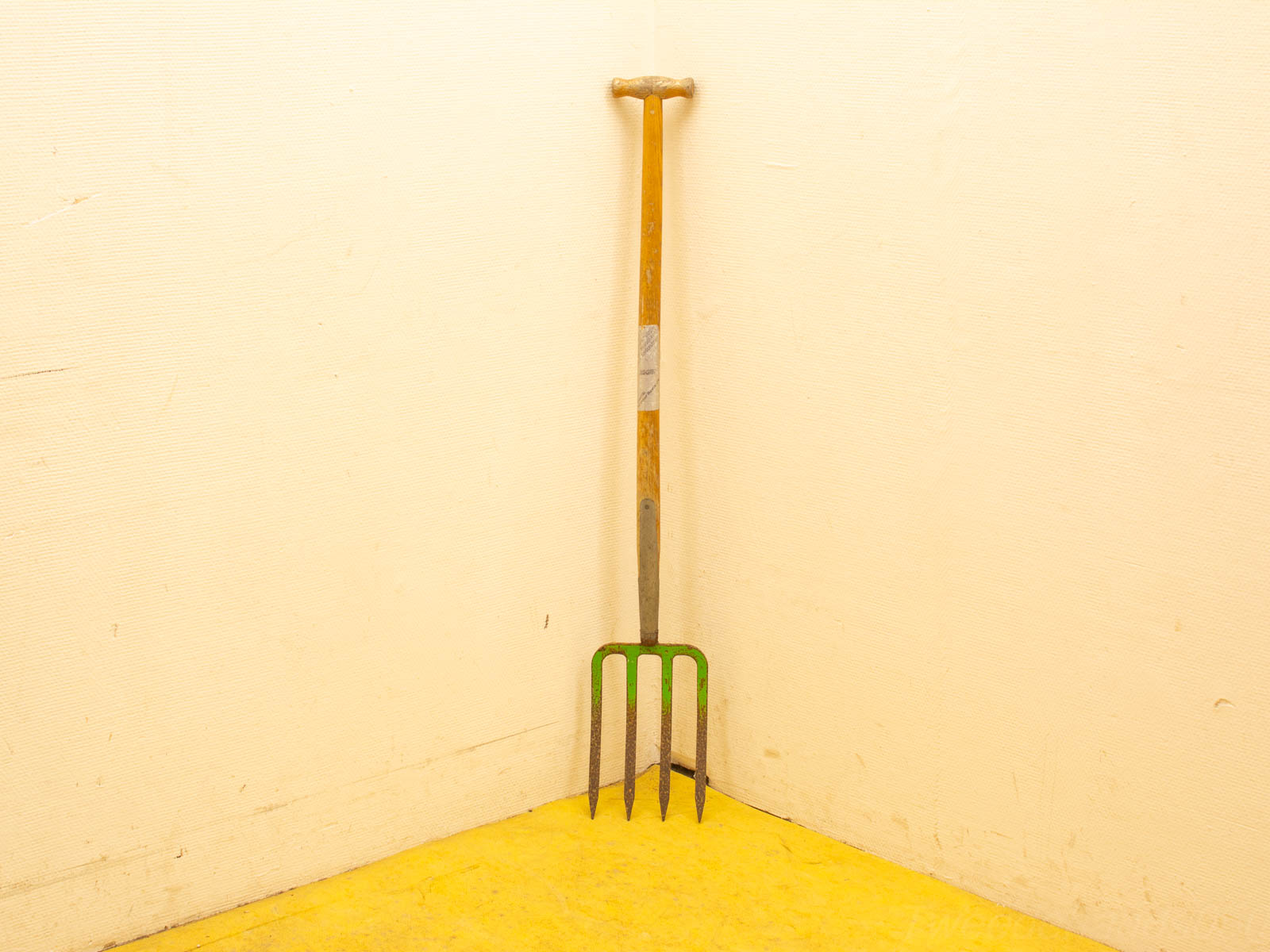 Rustic garden fork in a sunny yellow corner, embodying vintage charm and warmth.