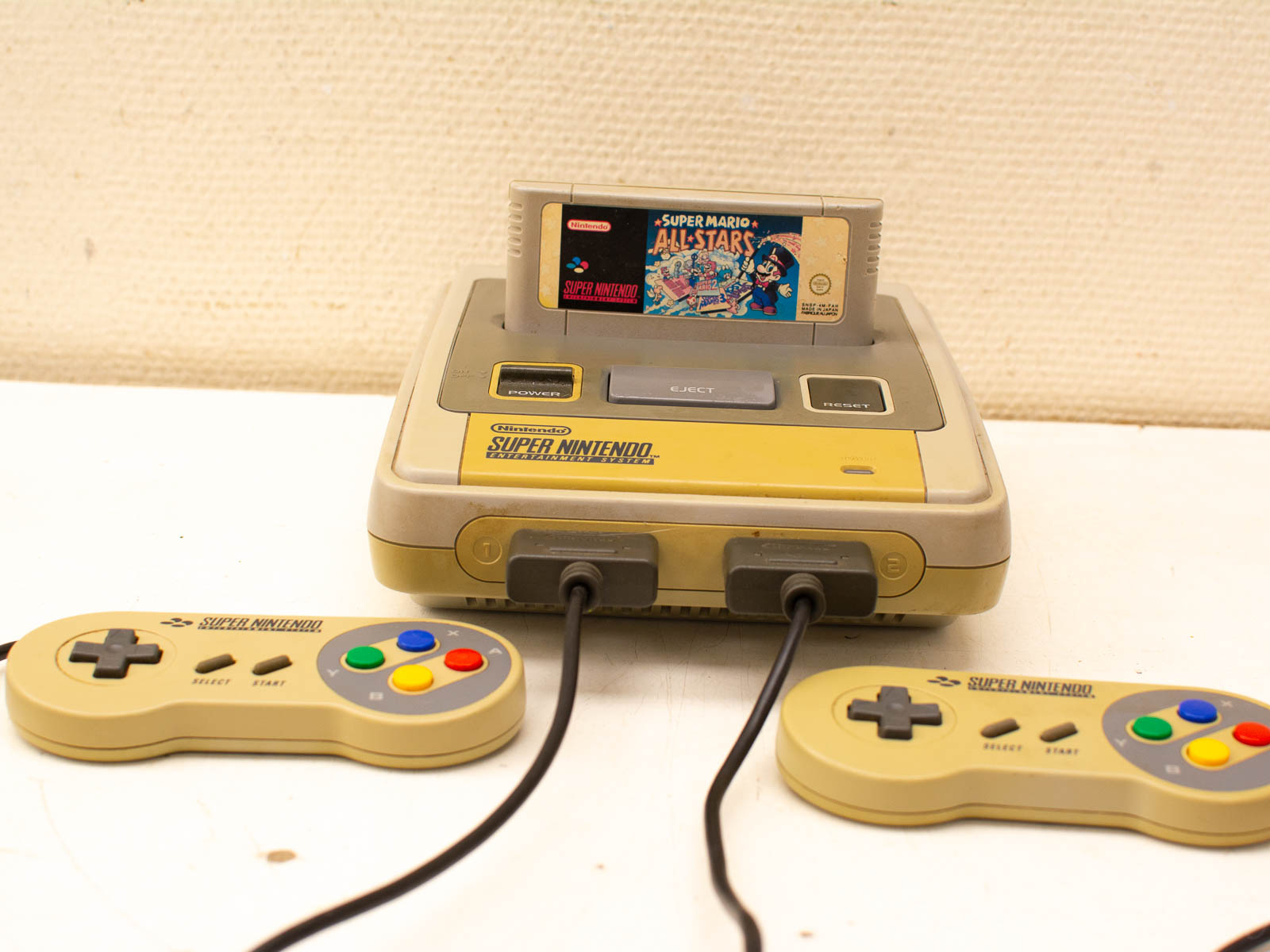 Classic Super Nintendo with Super Mario All-Stars cartridge and colorful controllers, evoking 90s gaming nostalgia.