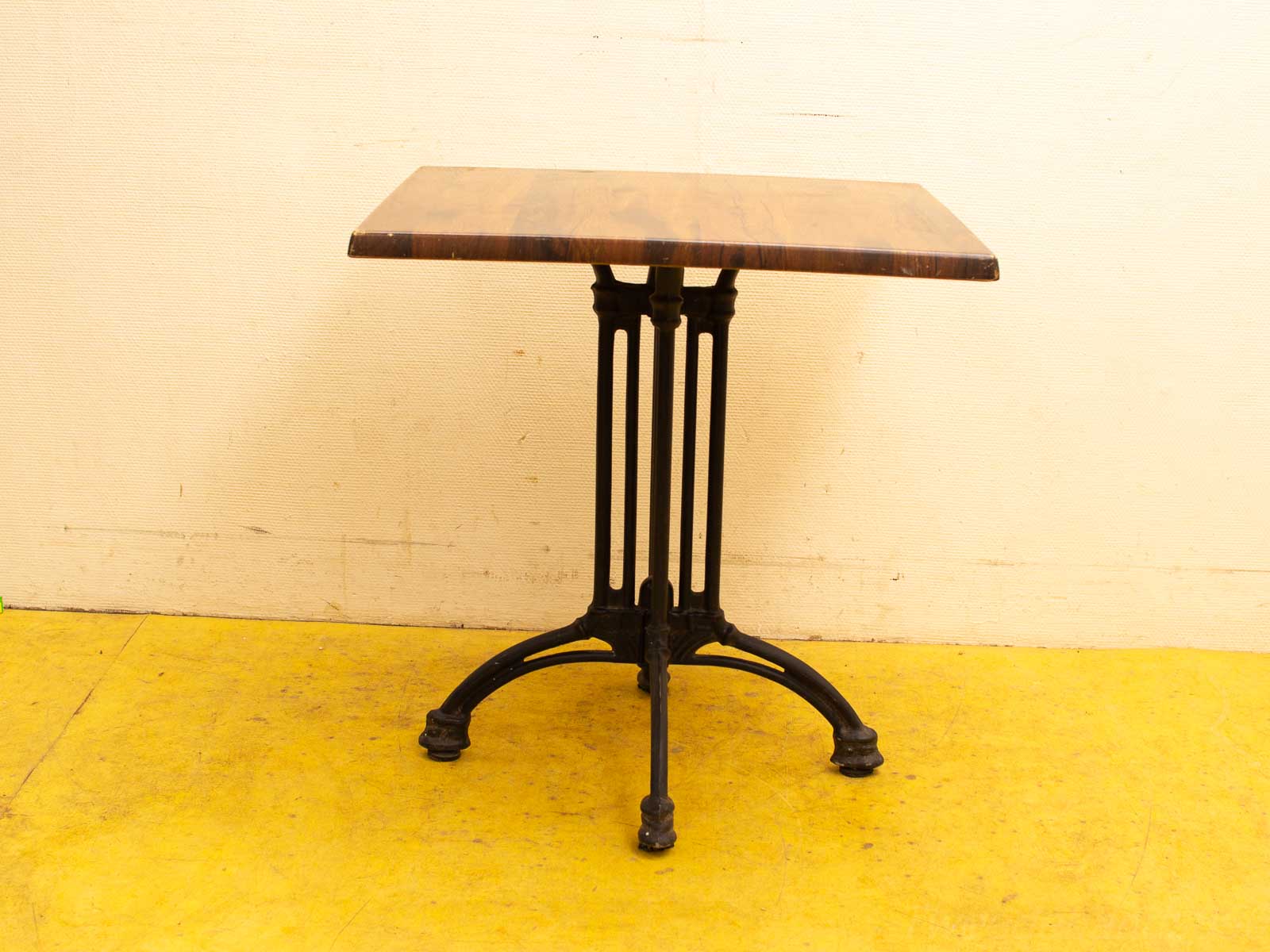 Elegant wooden table with a black iron base on a bright yellow floor.