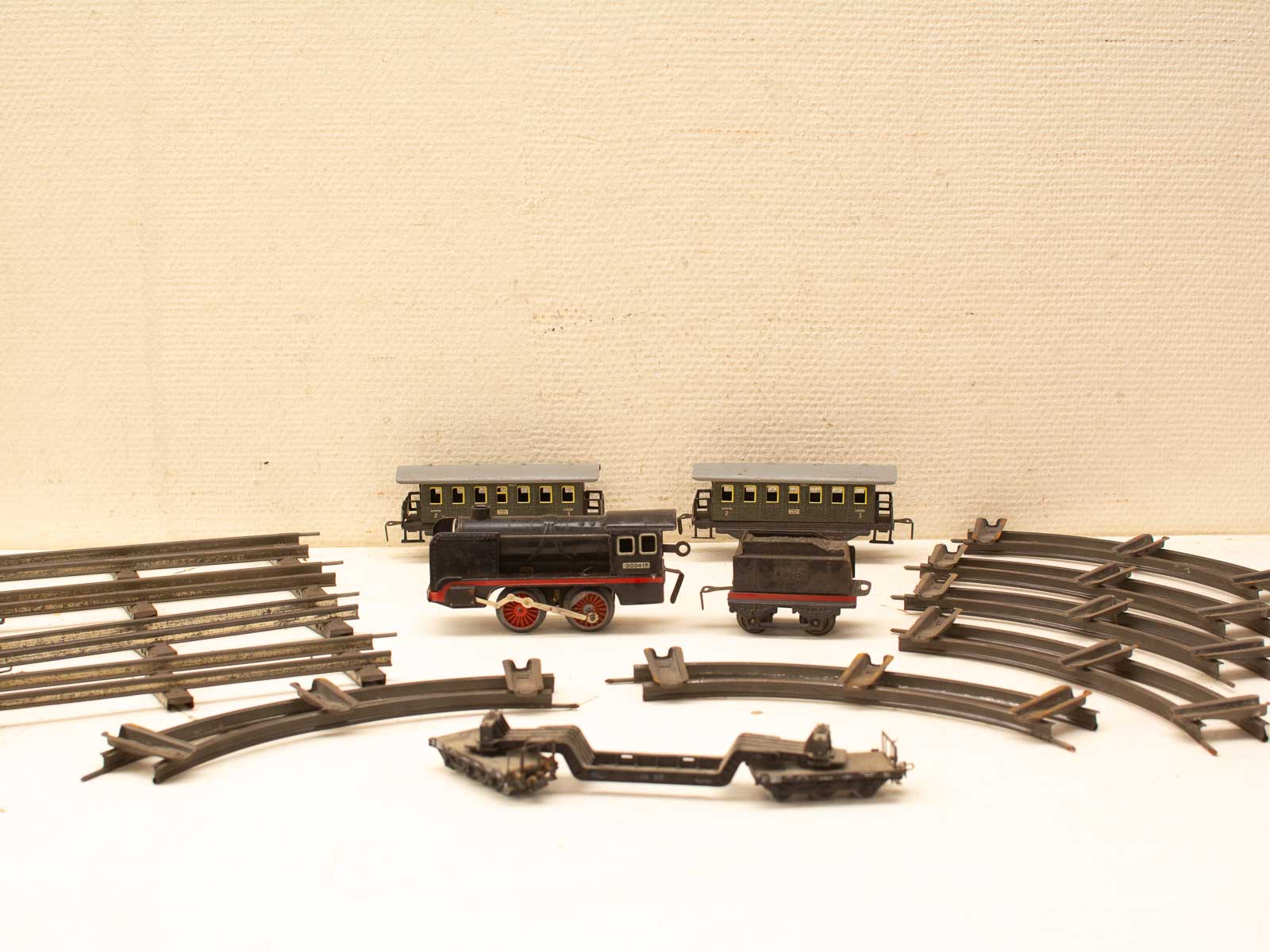 Vintage toy train set with black steam locomotive and green passenger car on weathered metal tracks.