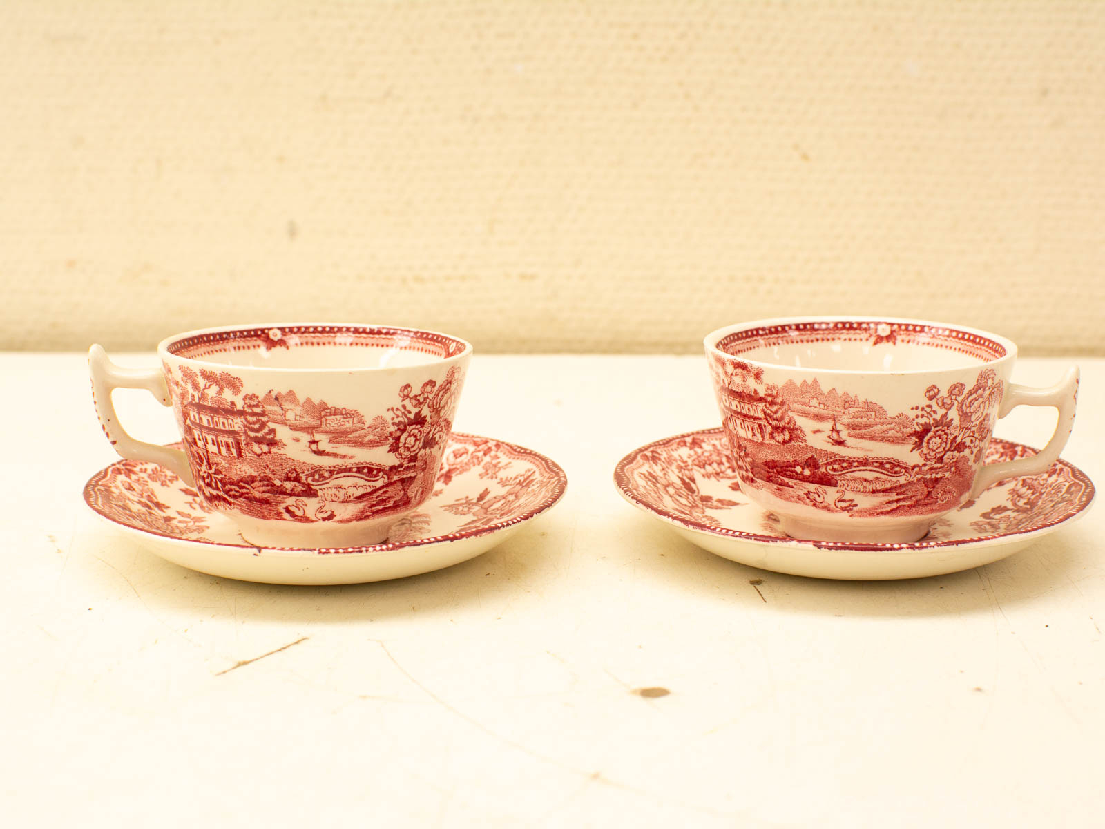 Charming red and white vintage porcelain teacups and saucers with intricate pastoral designs.