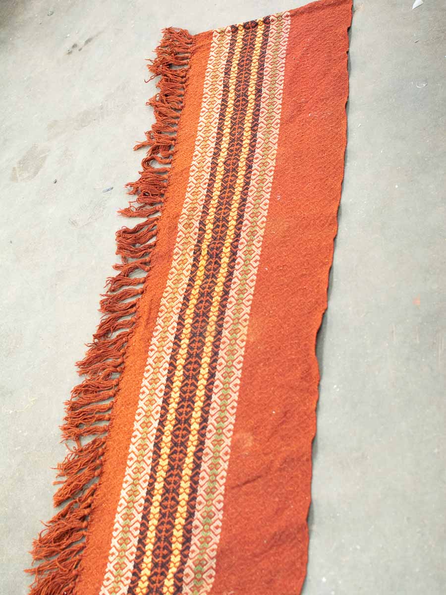 Handwoven terracotta textile with geometric patterns and playful fringes for artistic home decor.