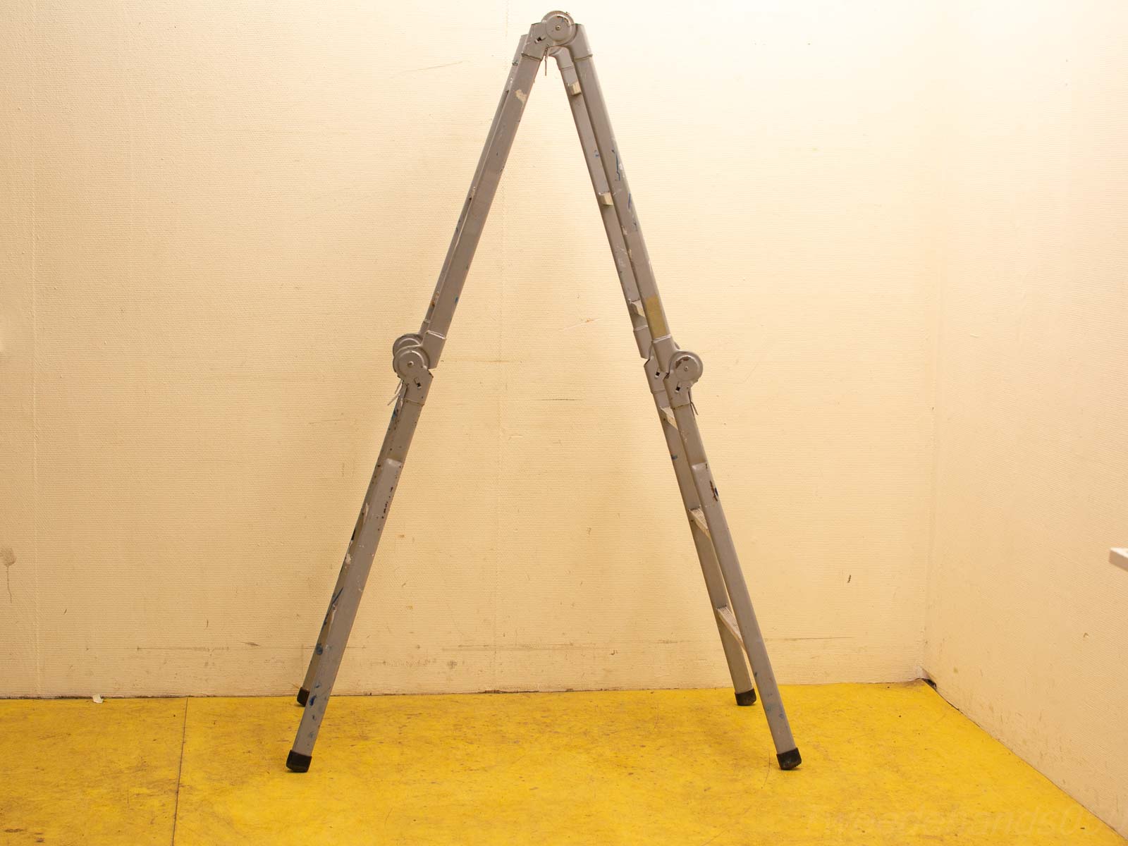 Vintage gray ladder against beige wall on vibrant yellow floor, perfect for any task.