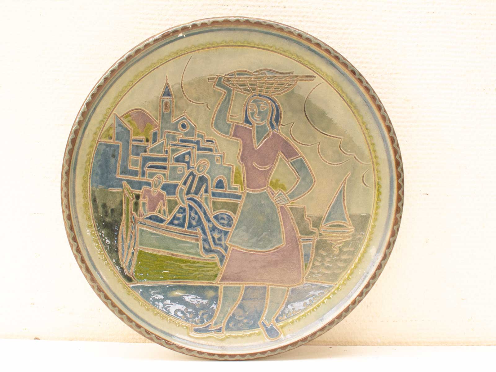 Vintage plate showcasing coastal life with a woman balancing a basket in vibrant relief design.