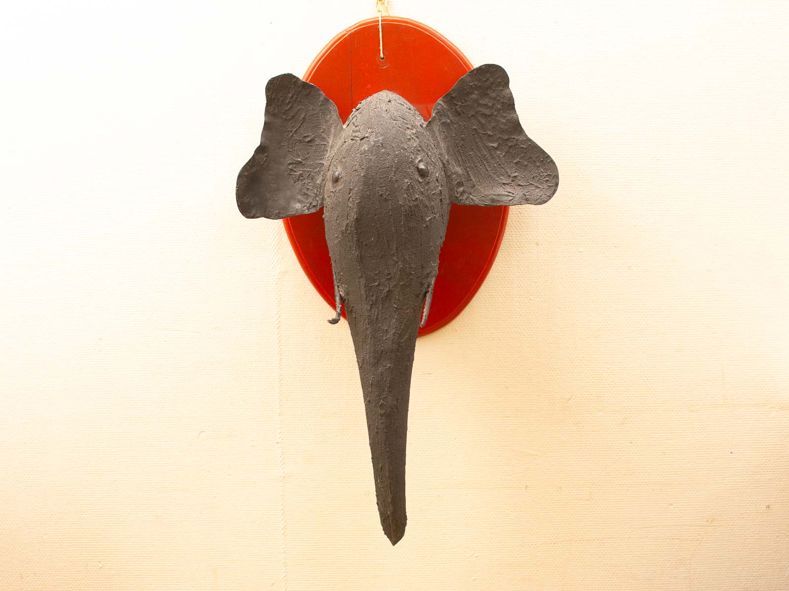 Handcrafted black elephant head wall sculpture with vivid reddish-orange mount against a neutral background.