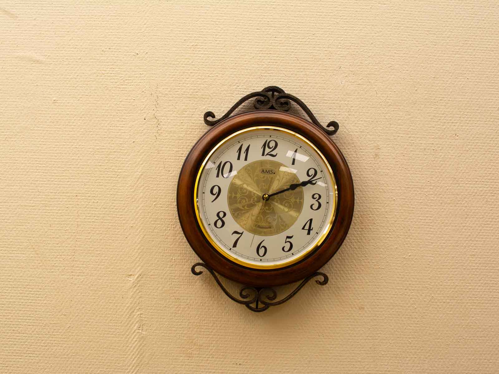 Elegant vintage wall clock with wooden frame and gold accents against a textured beige wall.