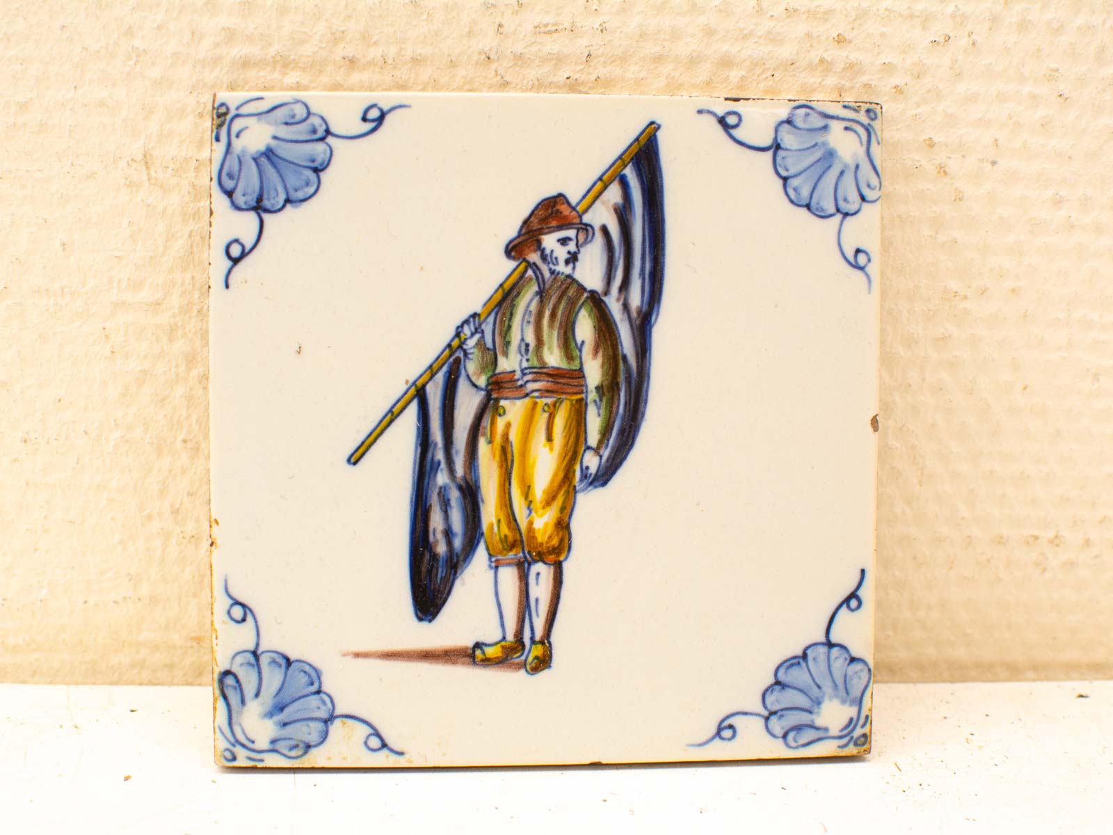 Hand-painted traditional tile featuring a colorful folkloric figure and intricate blue motifs.