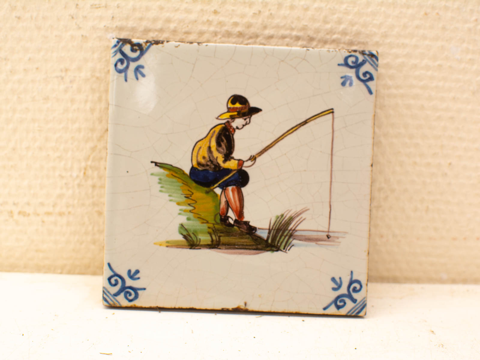 Vintage hand-painted tile featuring a charming scene of a young boy fishing in nature.