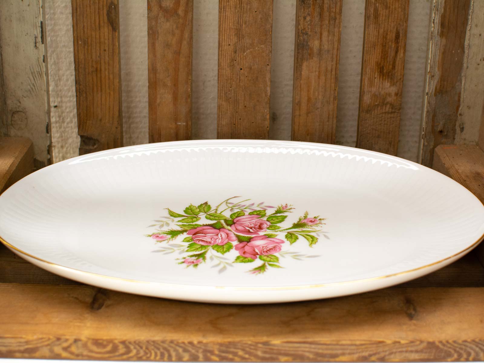 Elegant porcelain platter with pink roses and golden rim, set against a rustic wooden background.