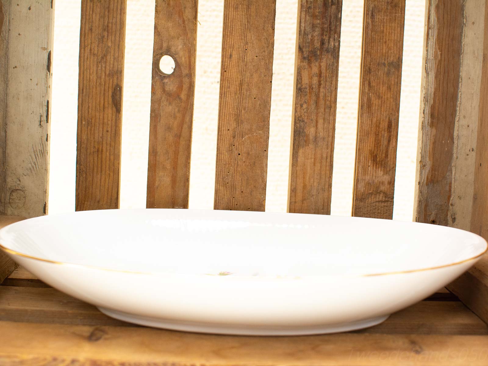 Elegant white ceramic dish with gold rim on rustic wooden surface, perfect for dining or decor.