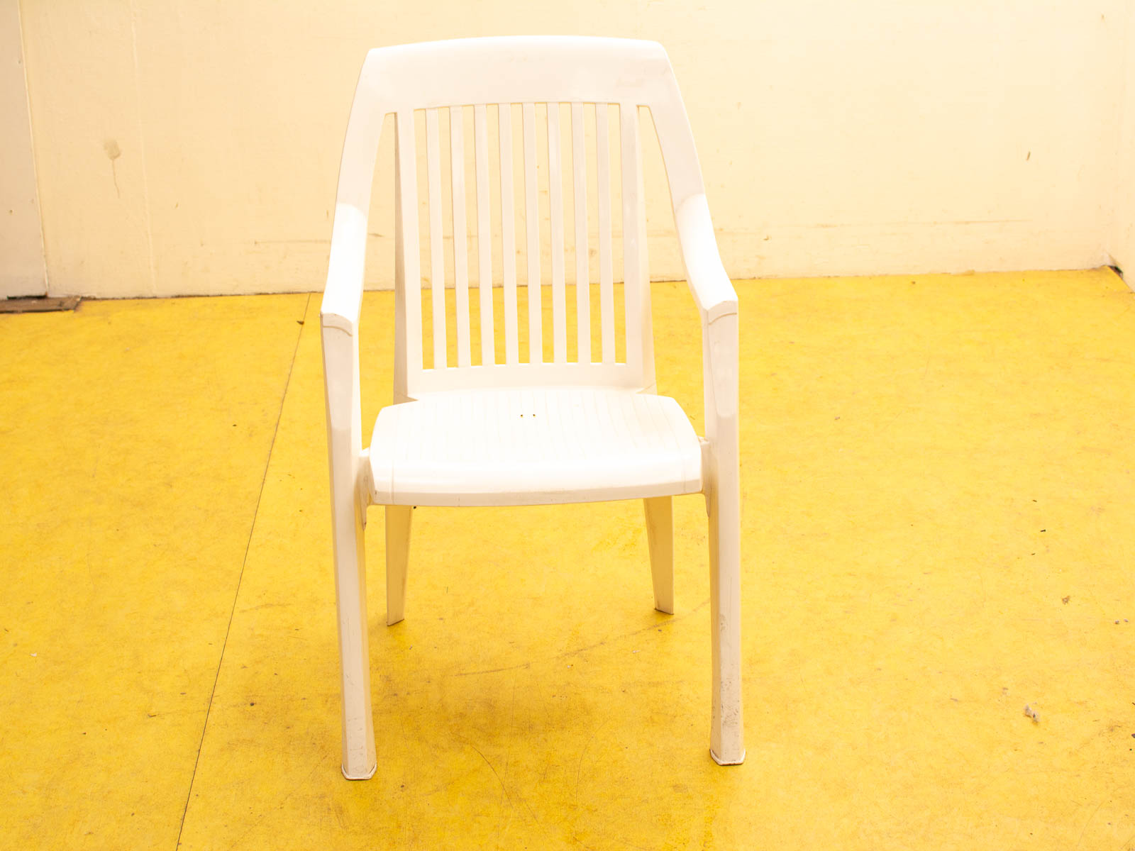 White plastic chair on bright yellow floor, showcasing simple design and lively contrast.