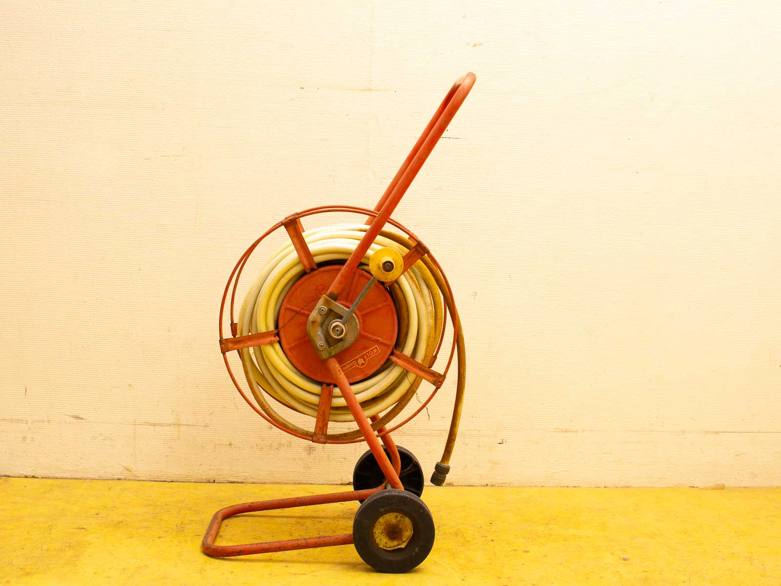 Charming vintage red metal hose reel with wheels, perfect for gardening and outdoor decor.